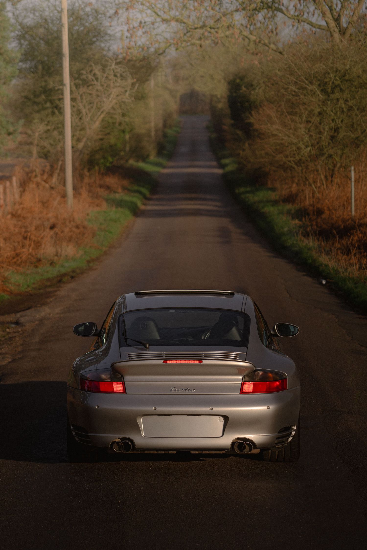 Silver Porsche 911 Turbo viewed from rear on a misty rural country lane at dusk.