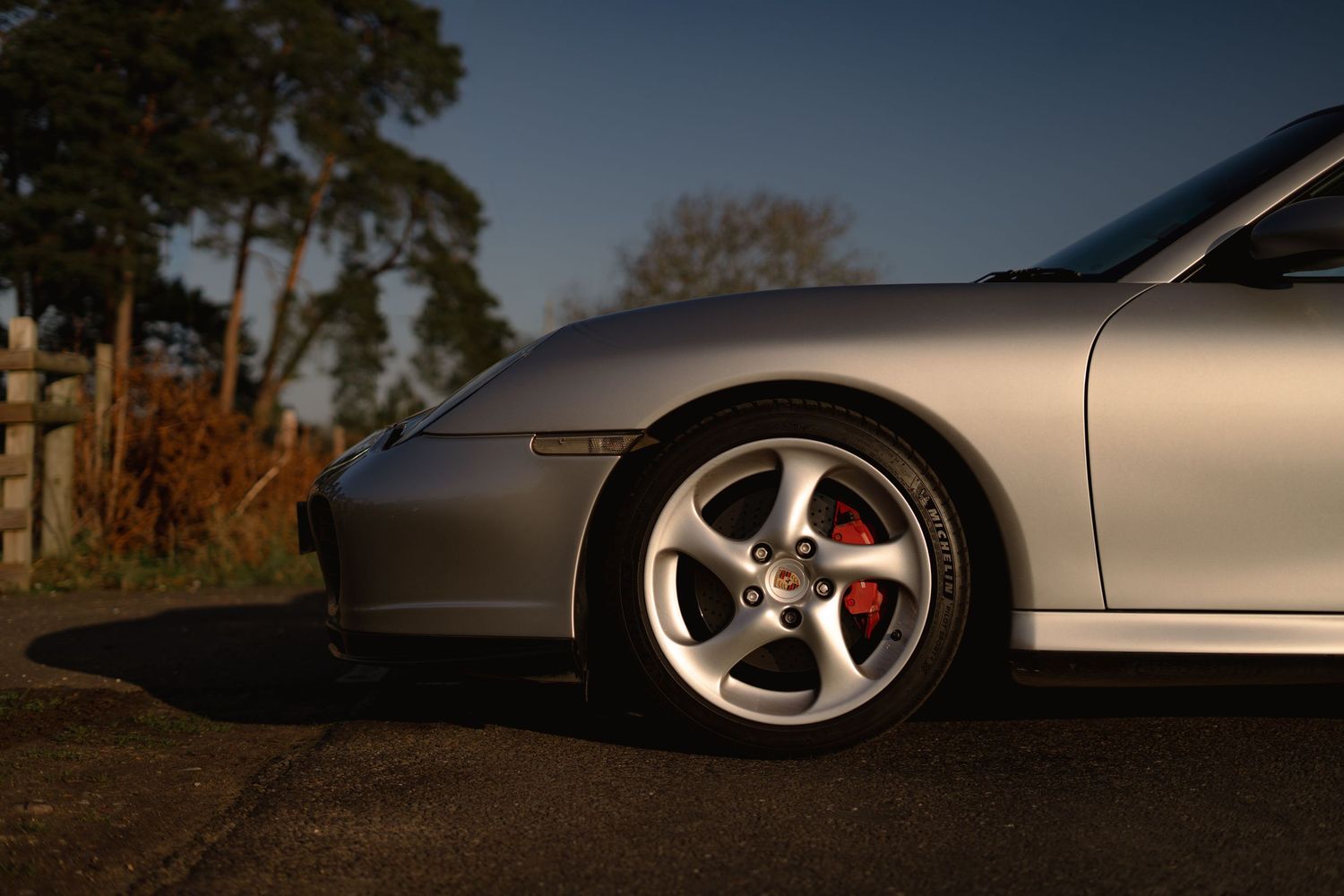 Low angle view of silver Porsche 911 alloy wheel with red brake caliper at twilight outdoors.