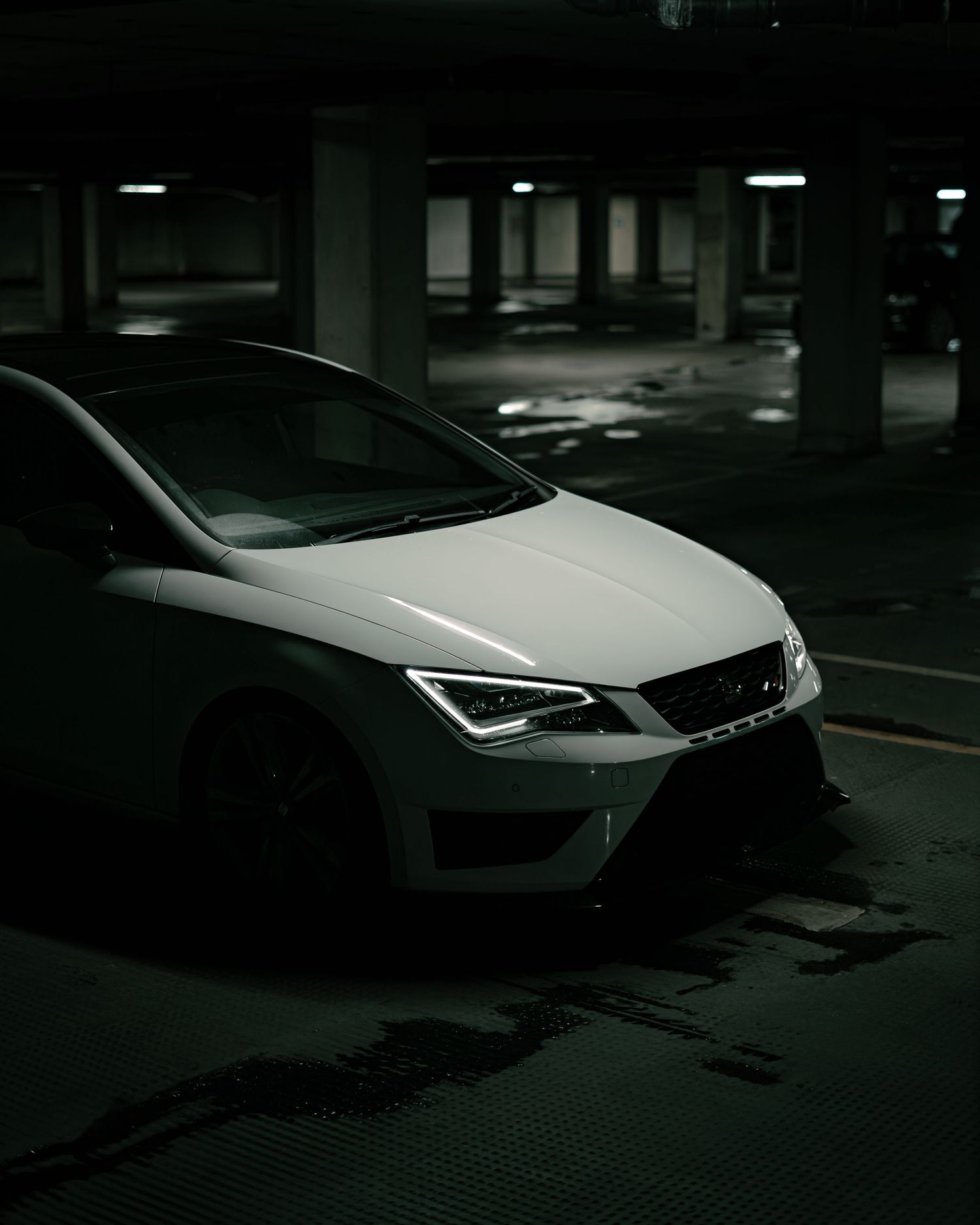 White sports car with aggressive front bumper in a dark underground parking garage.