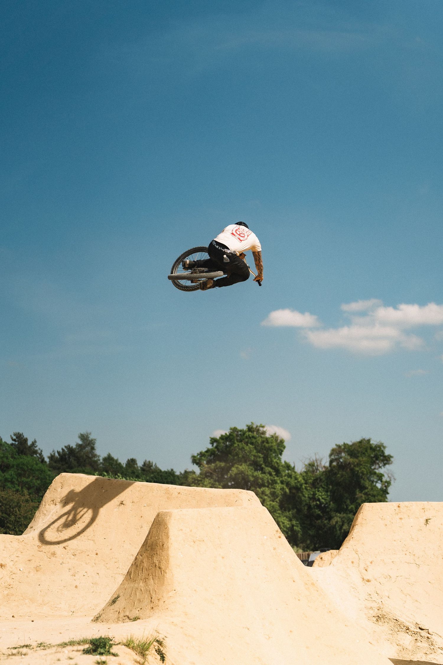 BMX rider executing an aerial trick high above sandy dirt jumps against a clear blue sky.