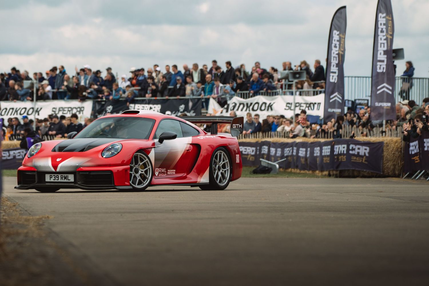 Red Porsche 911 GT3 RS performing at a motorsport event with Hankook-sponsored banners and a large crowd.