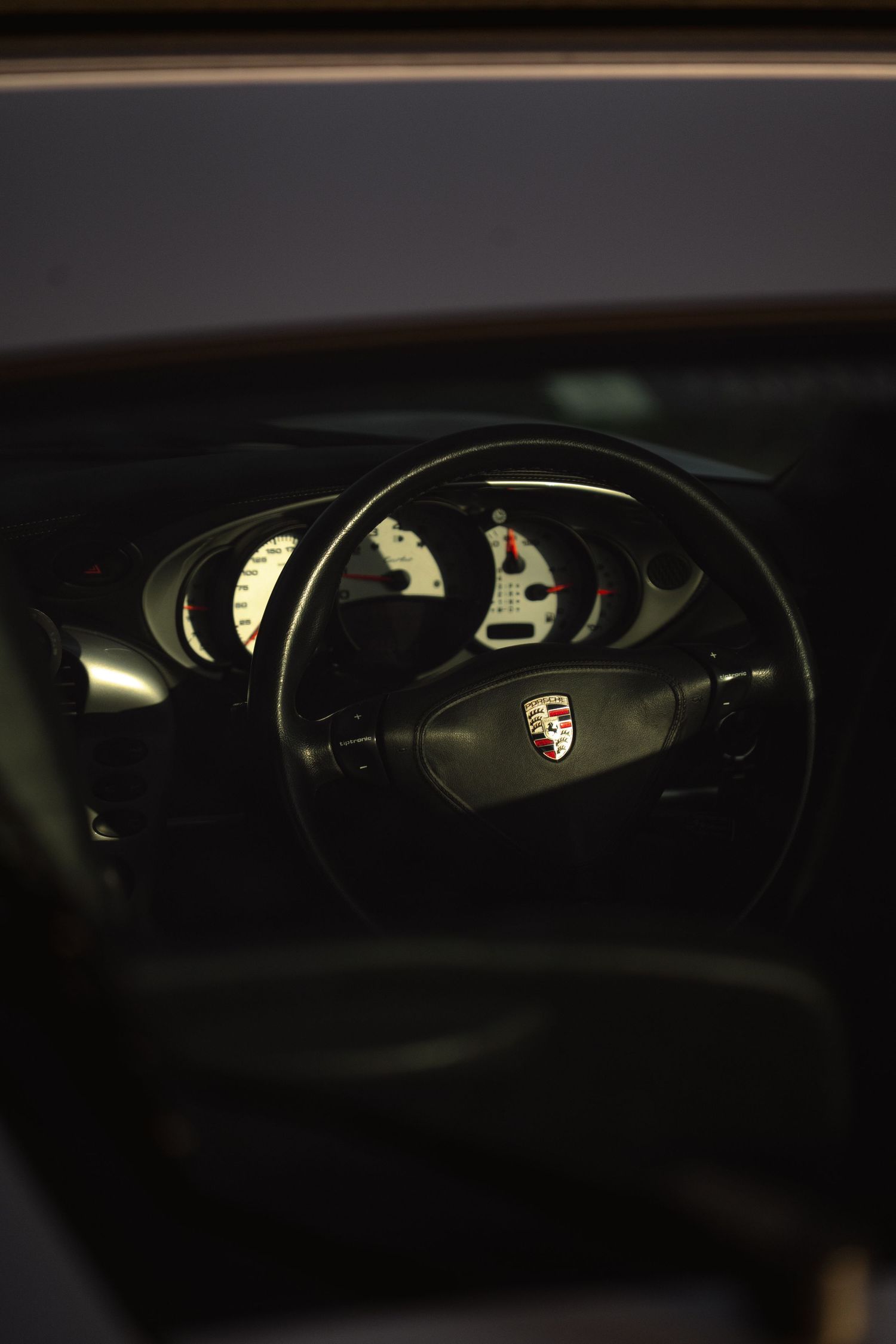 Porsche 911 Turbo steering wheel and instrument cluster viewed through window.