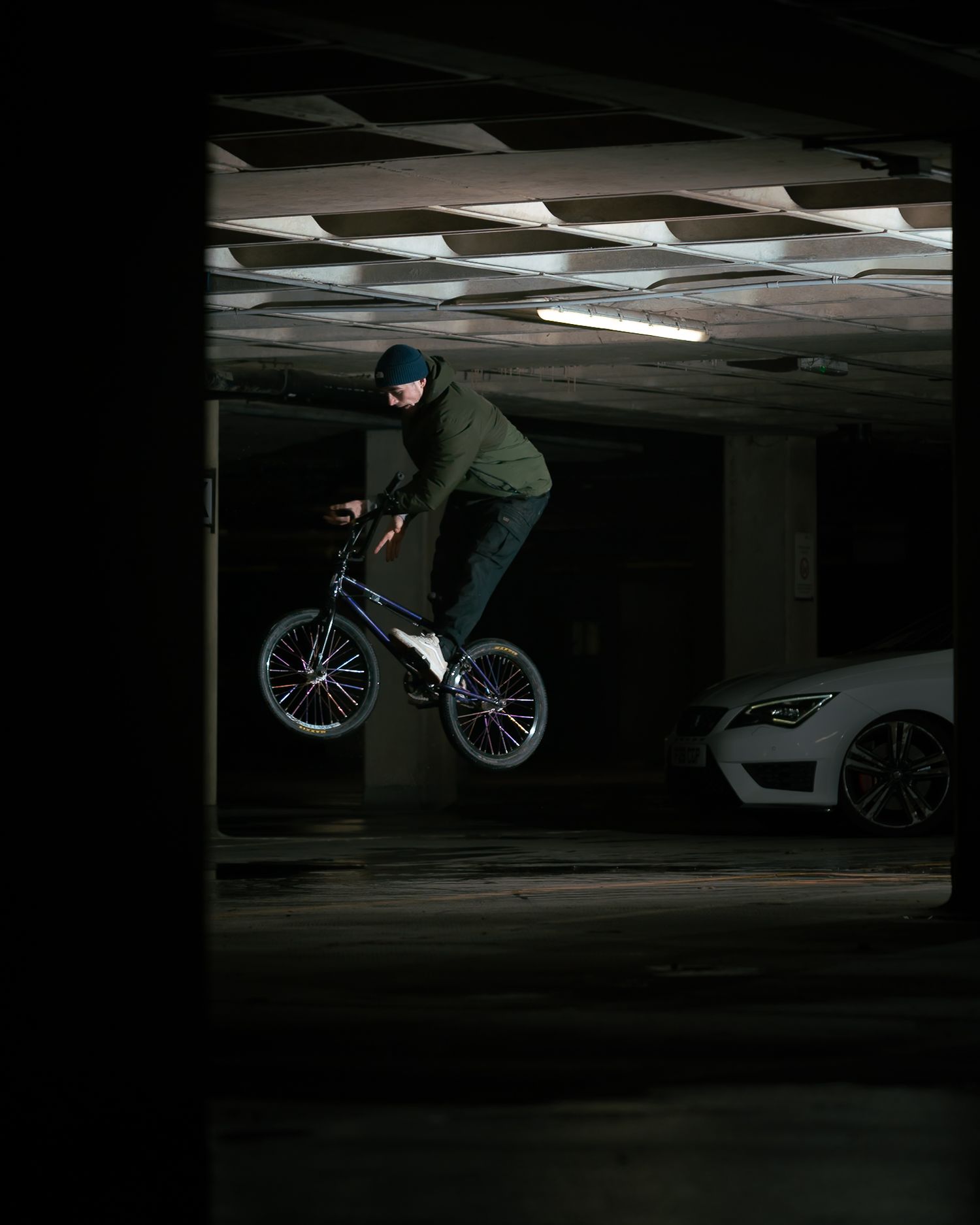 BMX rider performing a jump trick inside a dark parking garage with a white car in the background.