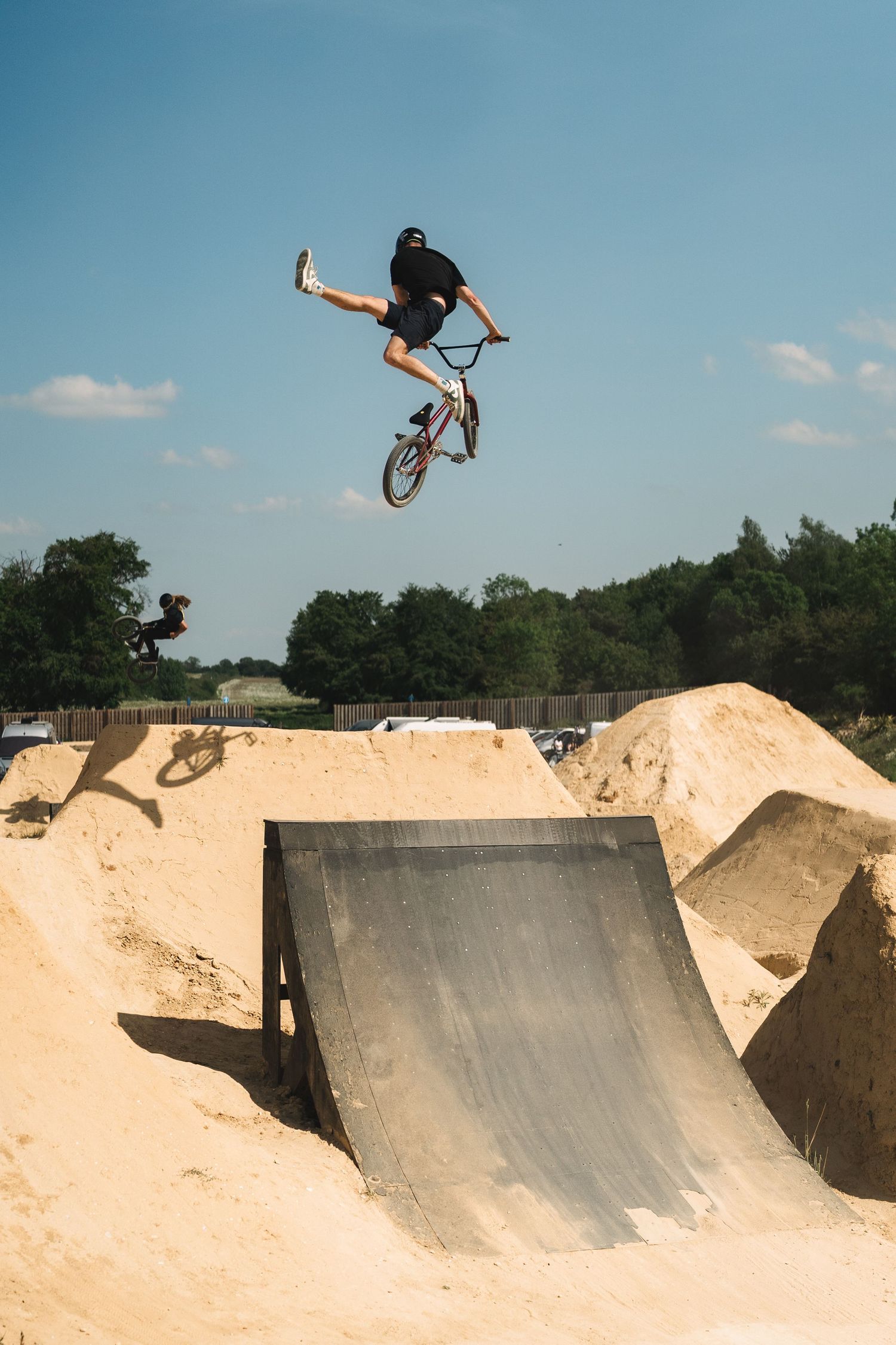 BMX rider executes an aerial trick above a sandy skate park ramp on a sunny day.