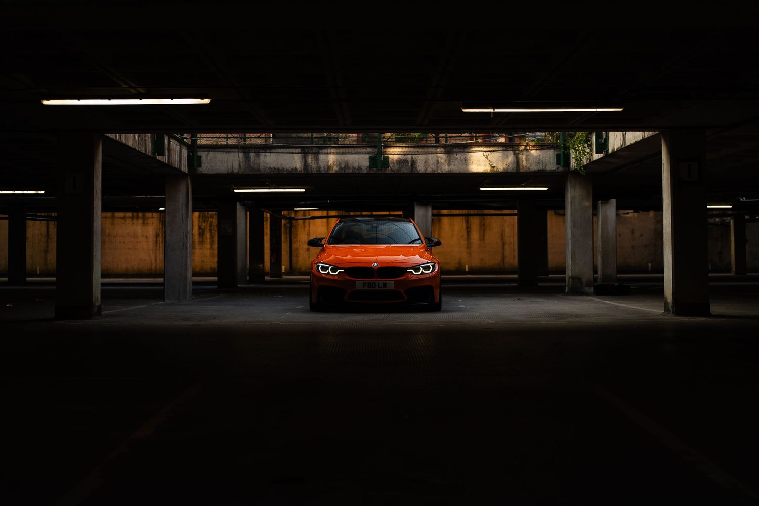 Orange sports car parked in a dark parking garage, illuminated by overhead lights, front view.