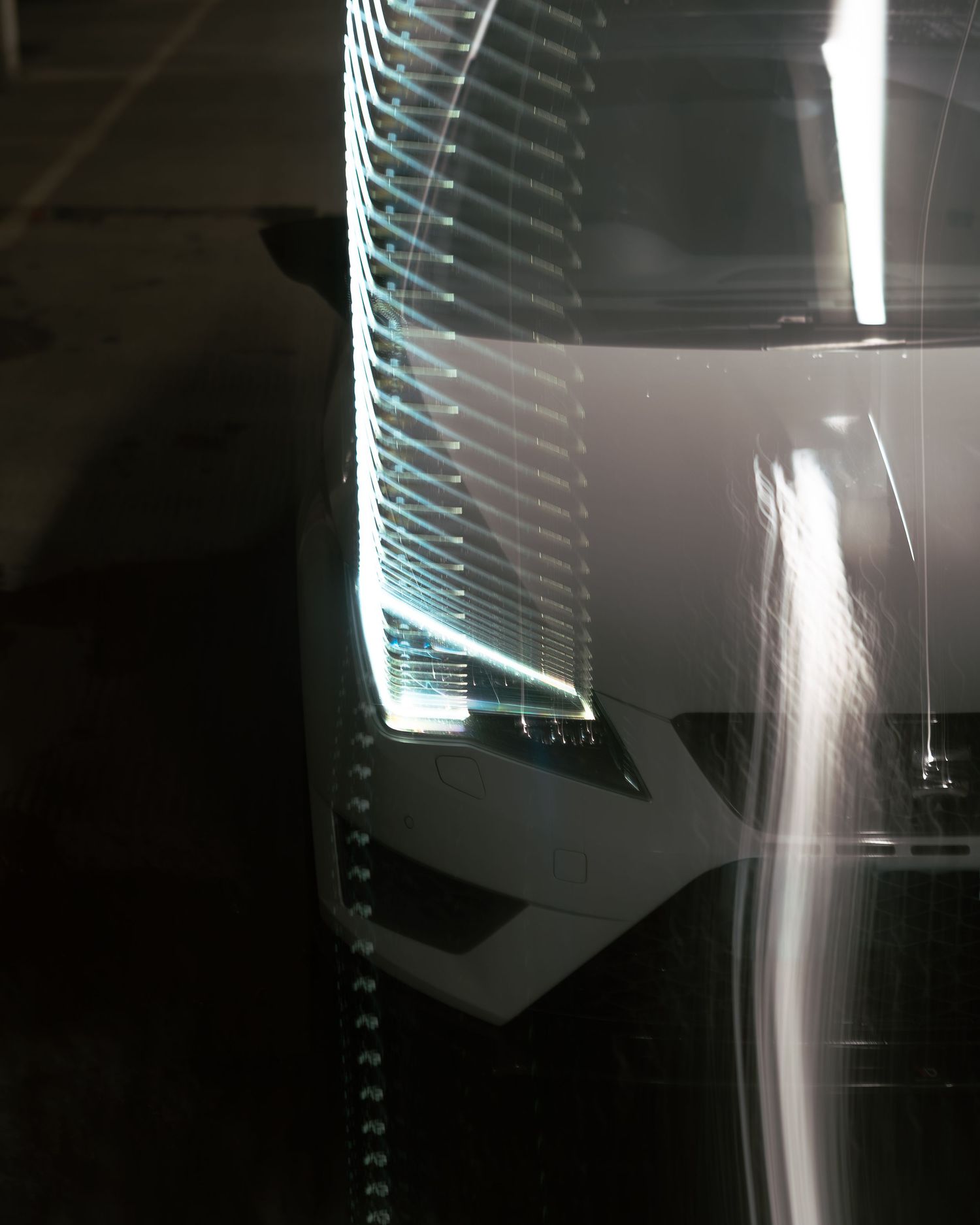 Close-up of a white sports car headlight with LED daytime running lights in a dark parking garage.