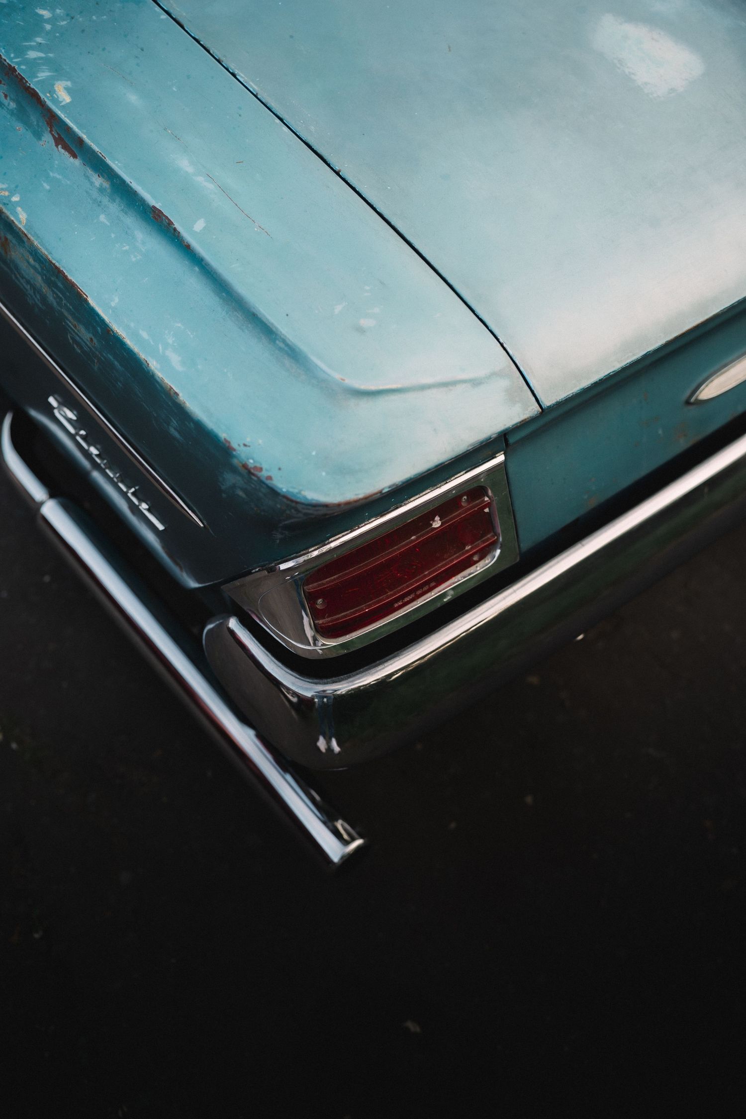 Close-up of a vintage turquoise car rear with chrome trim and red tail light, showing aged patina paint.