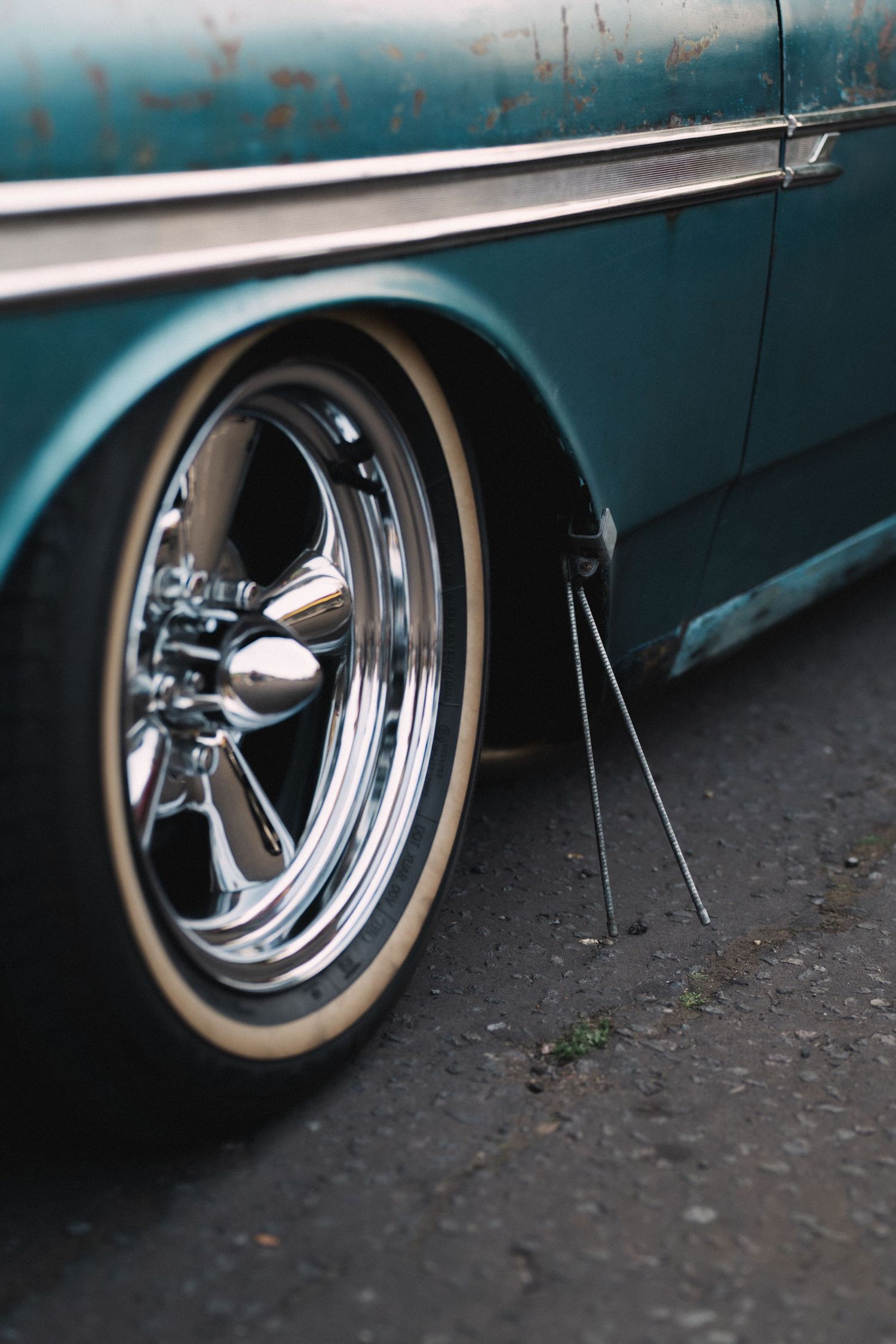 Close-up of a chrome five-spoke wheel with whitewall tire on a vintage teal classic car.