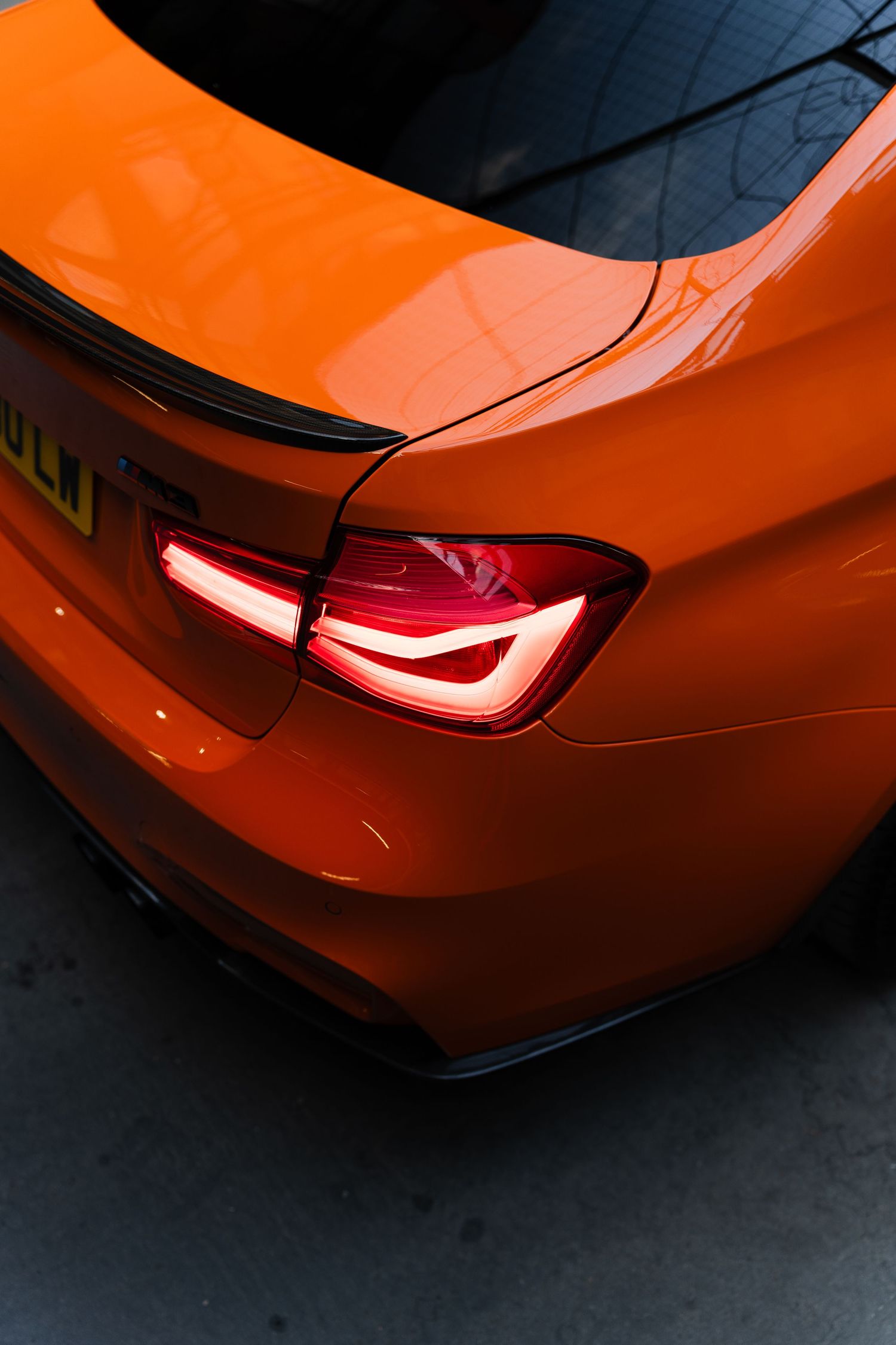 Close-up rear view of a vibrant orange BMW with glowing red LED tail lights and carbon fiber spoiler.
