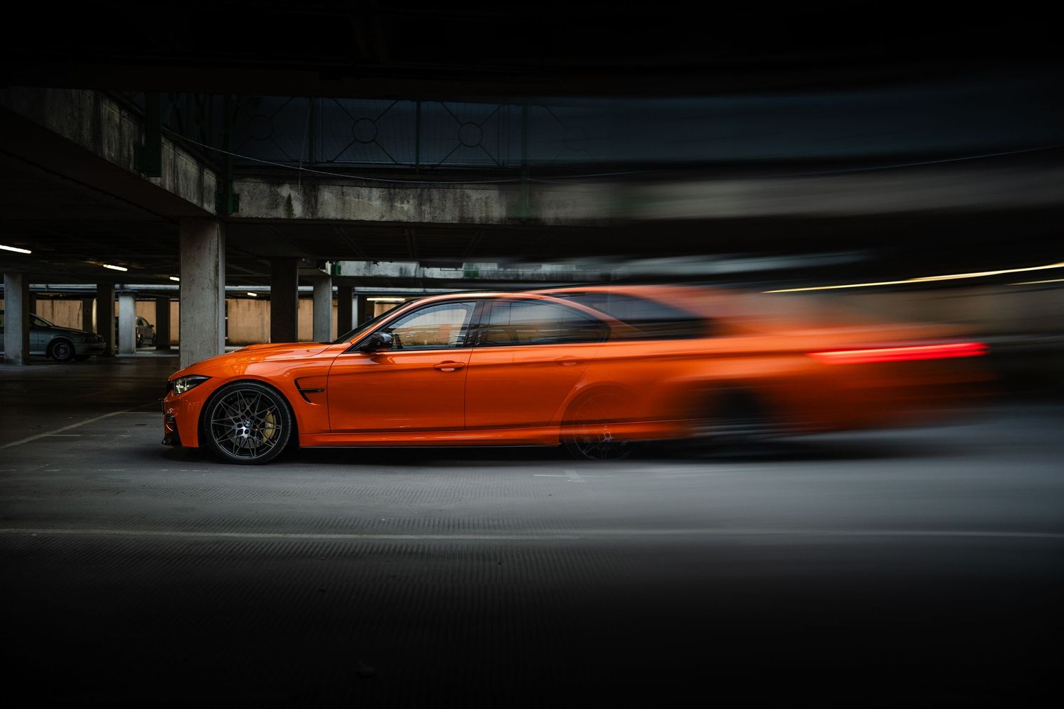 Orange BMW M4 speeding through a dark parking garage with motion blur effect highlighting its aggressive stance.