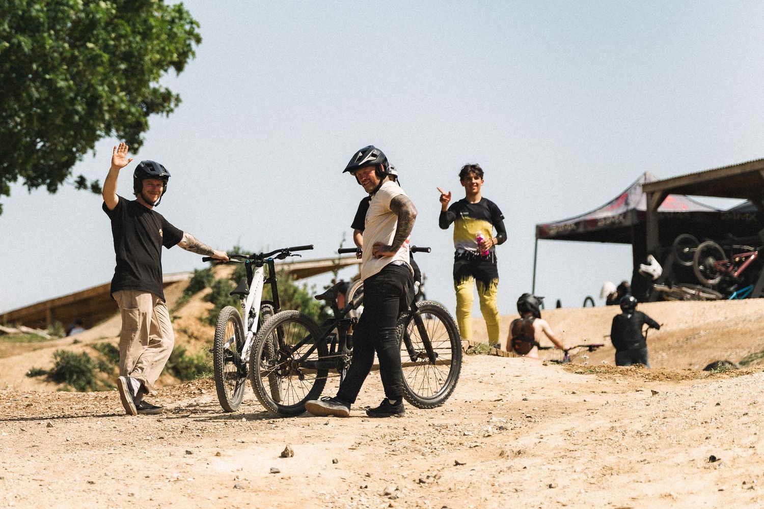 Four mountain bikers gather on a dusty trail, with two giving high fives near their bikes on a sunny day.