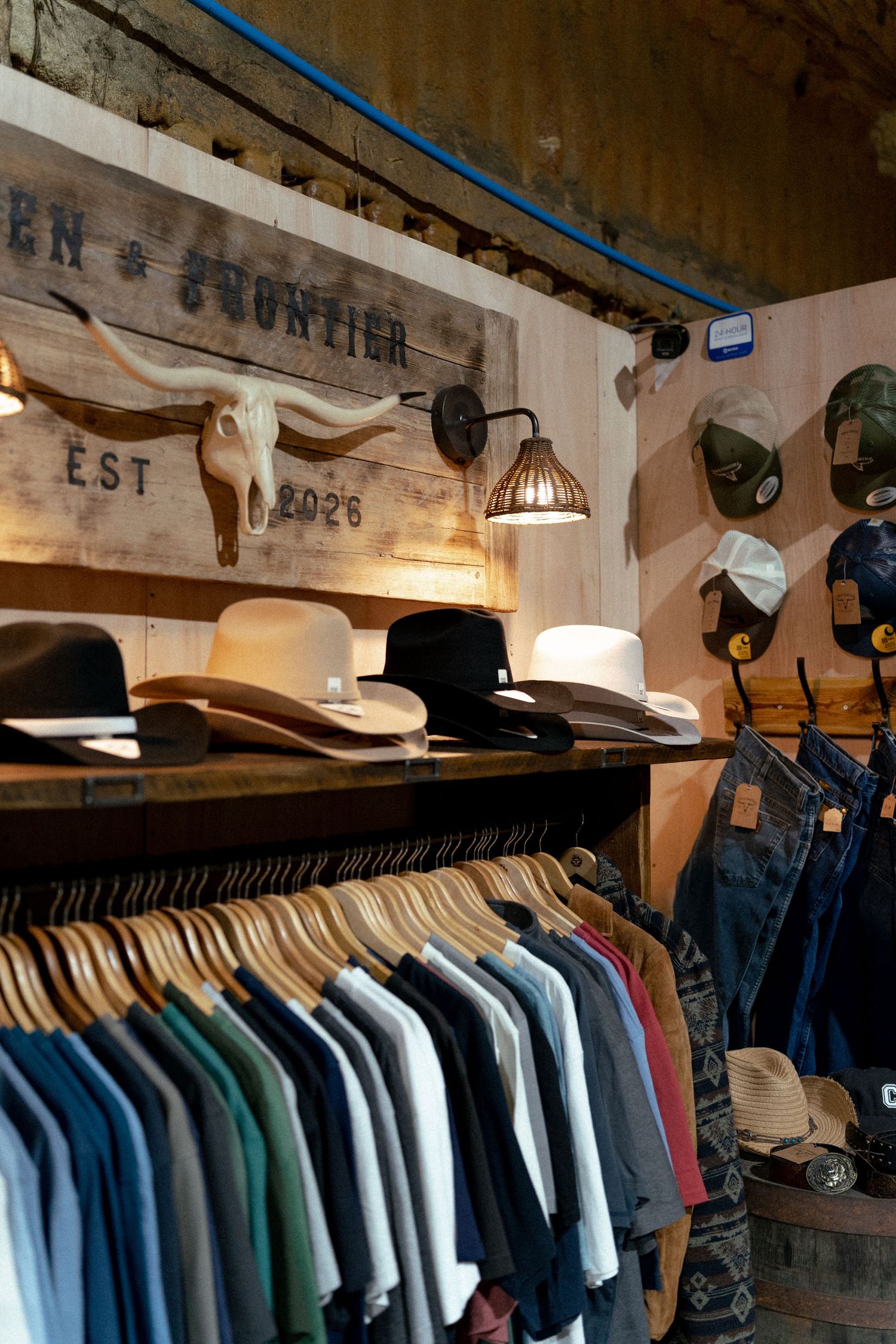 Western frontier store interior with cowboy hats, denim clothing on racks, and longhorn skull wall decor, EST 2026.