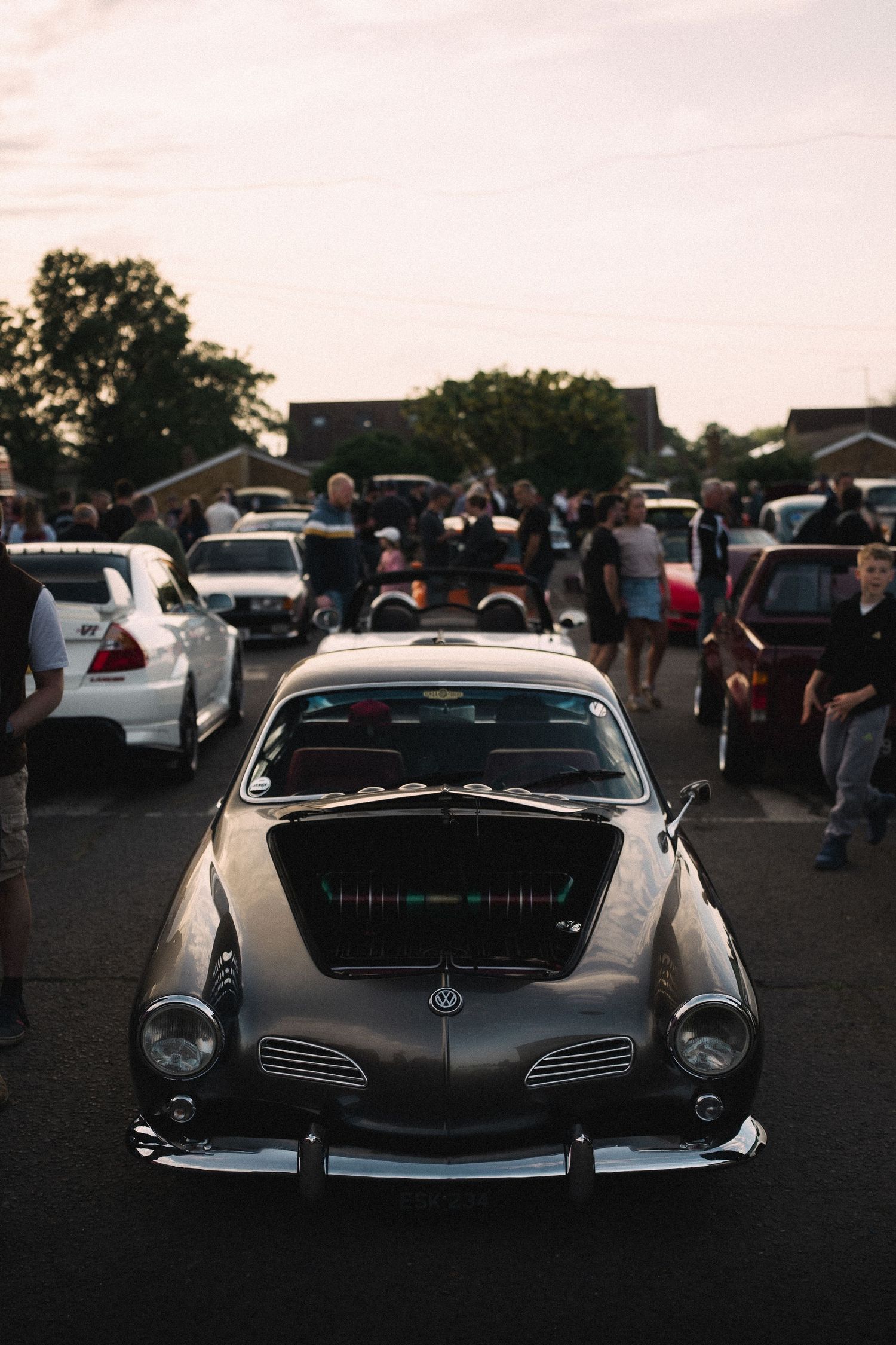 Vintage Volkswagen Karmann Ghia displayed at a classic car show during dusk with spectators in background.