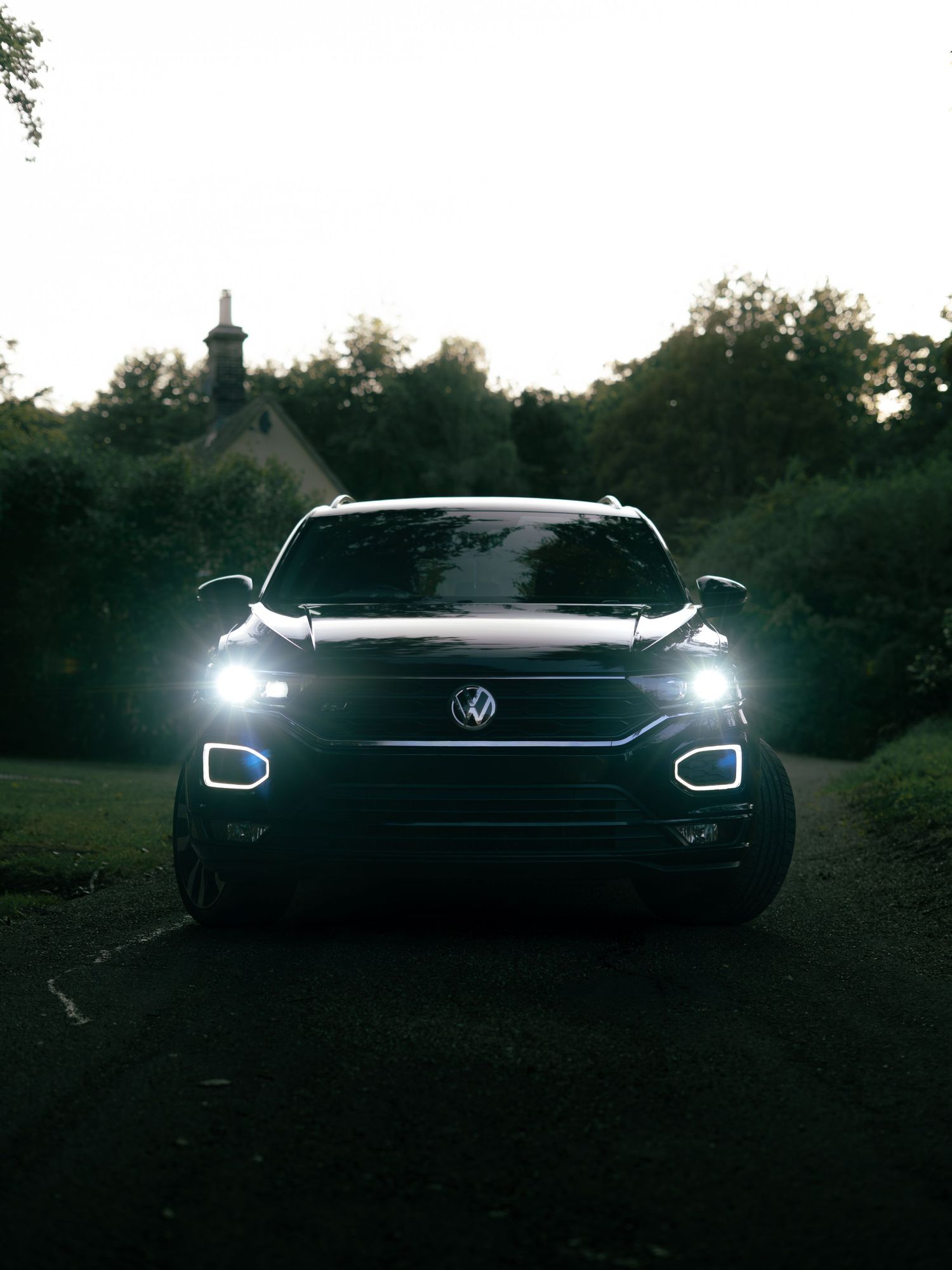 A Volkswagen T-Roc SUV with bright LED headlights parked on a dark road at dusk.