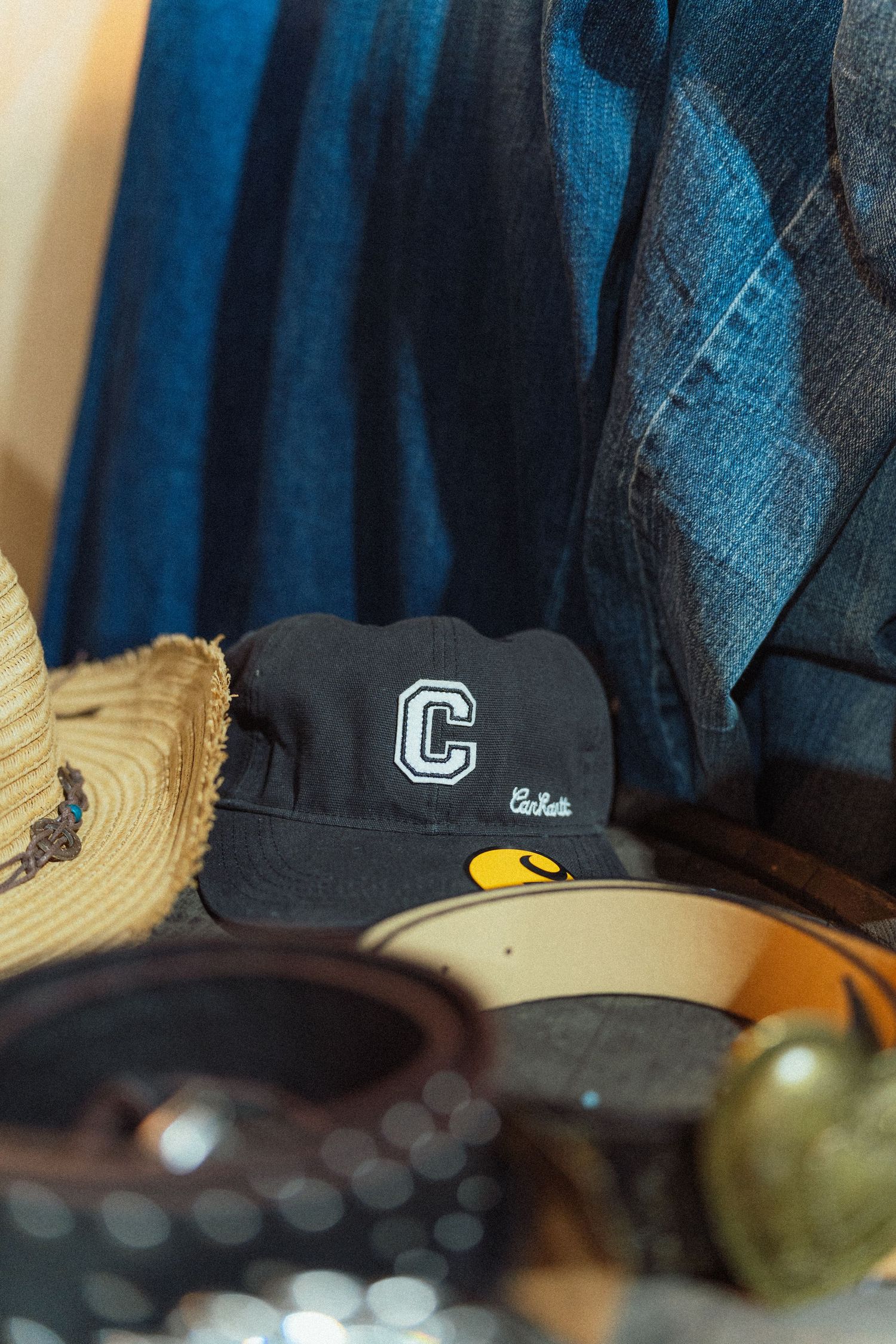 Collection of vintage hats, sunglasses, and denim clothing arranged together, featuring a black cap with letter C logo.