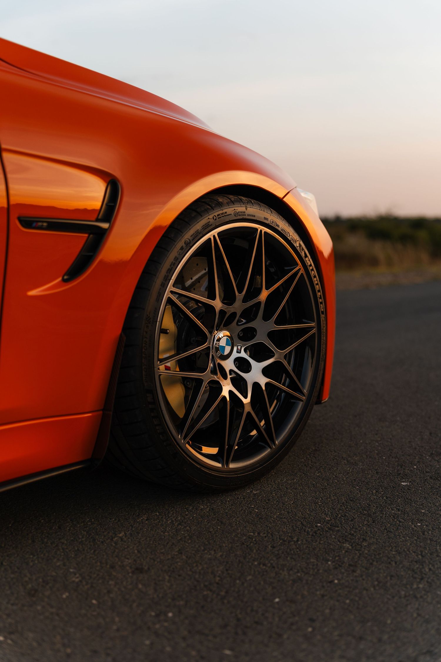 Orange BMW sports car with bronze multi-spoke alloy wheel on open road at sunset.