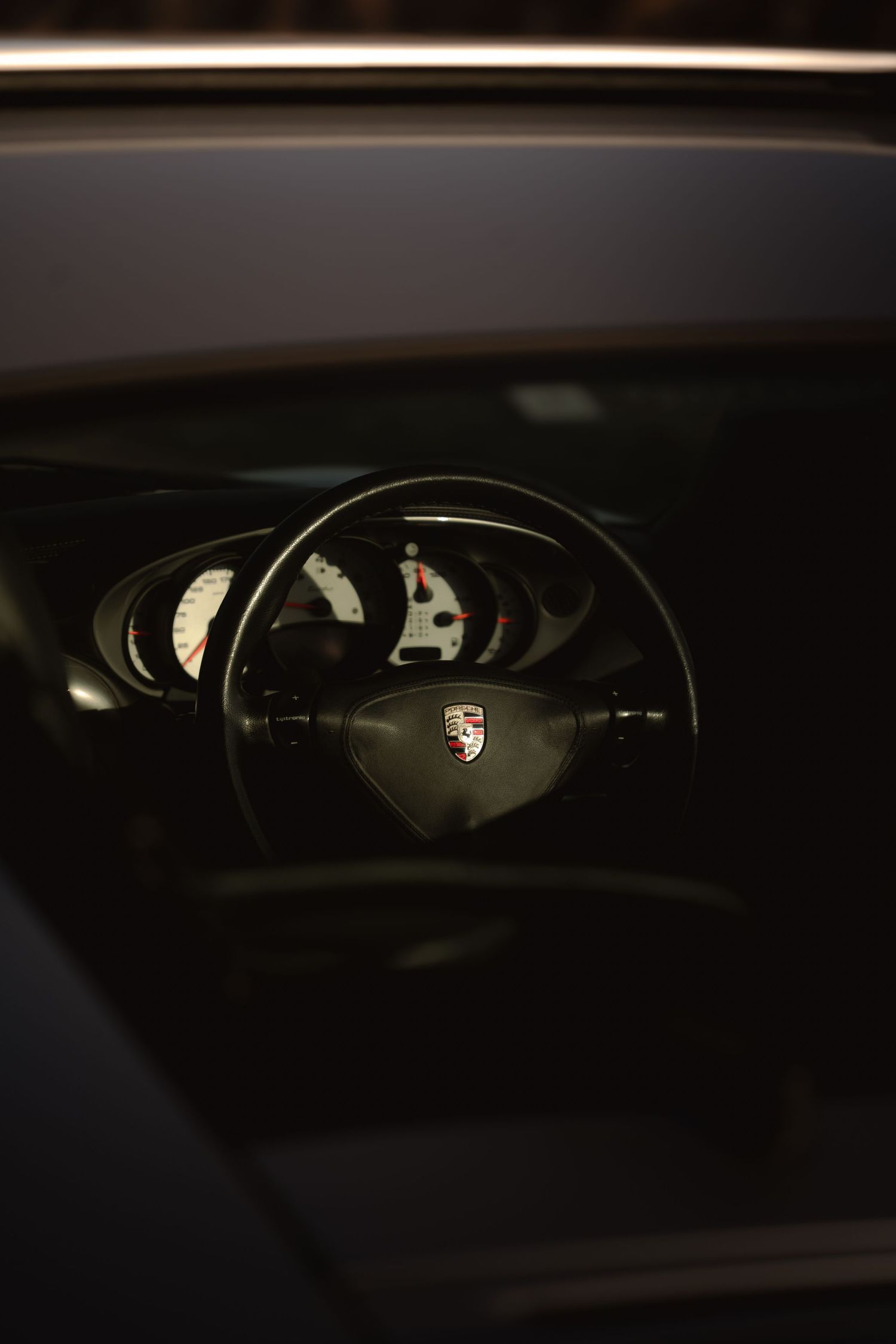 Porsche 911 Turbo steering wheel with crest badge and illuminated white gauges through window.
