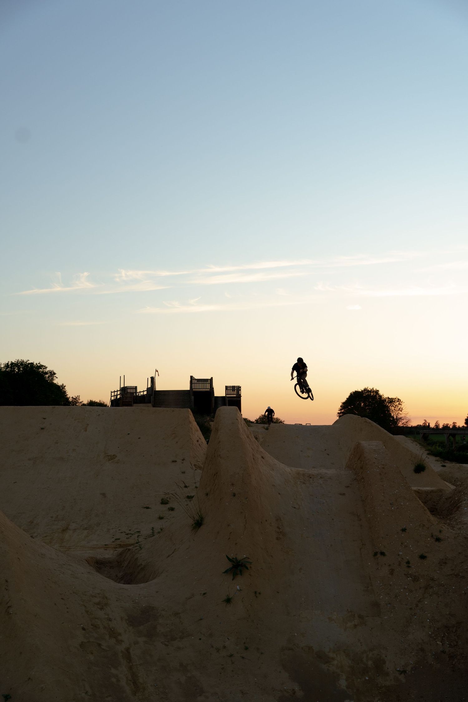 Silhouette of a BMX rider jumping over dirt mounds at a skate park during a golden sunset.