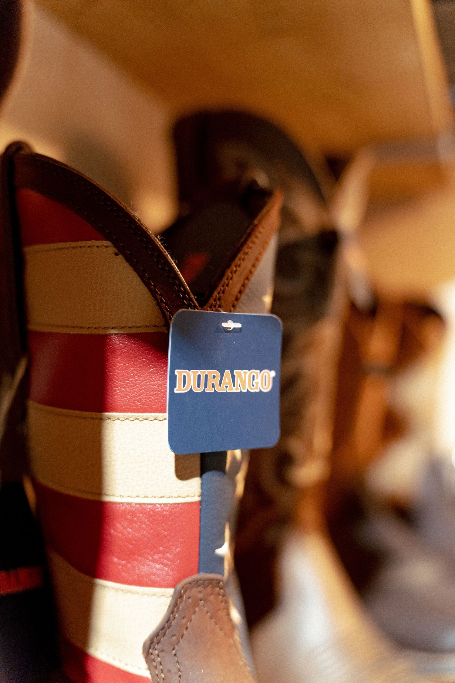 Durango brand cowboy boots with red, white, and brown leather stripes displayed on a store shelf with price tag.