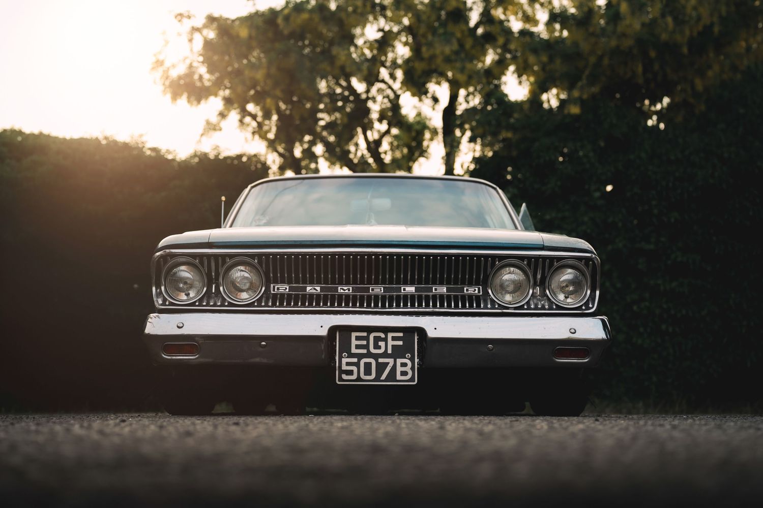 Vintage classic car with license plate EGF 507B parked outdoors at sunset with lush green trees in background.