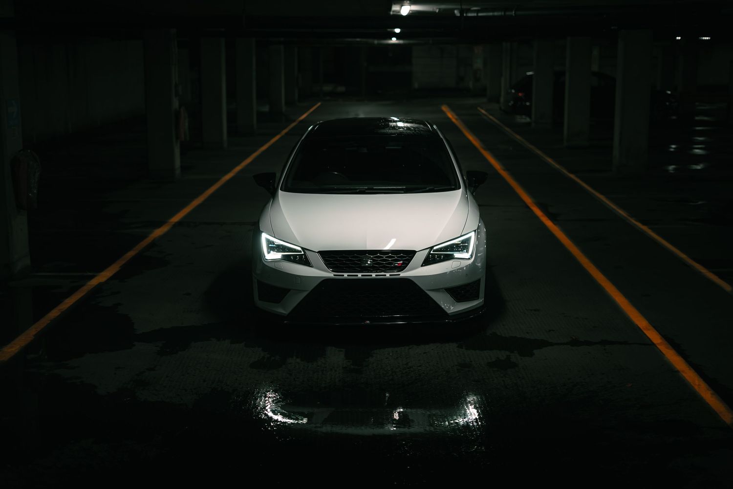 White SEAT Leon Cupra photographed from front in a dark underground parking garage with yellow lines.