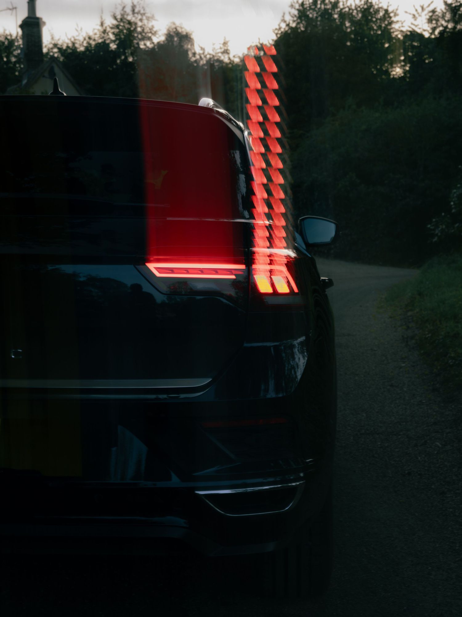Motion-blurred red LED tail light of a black SUV on a rural road at dusk.