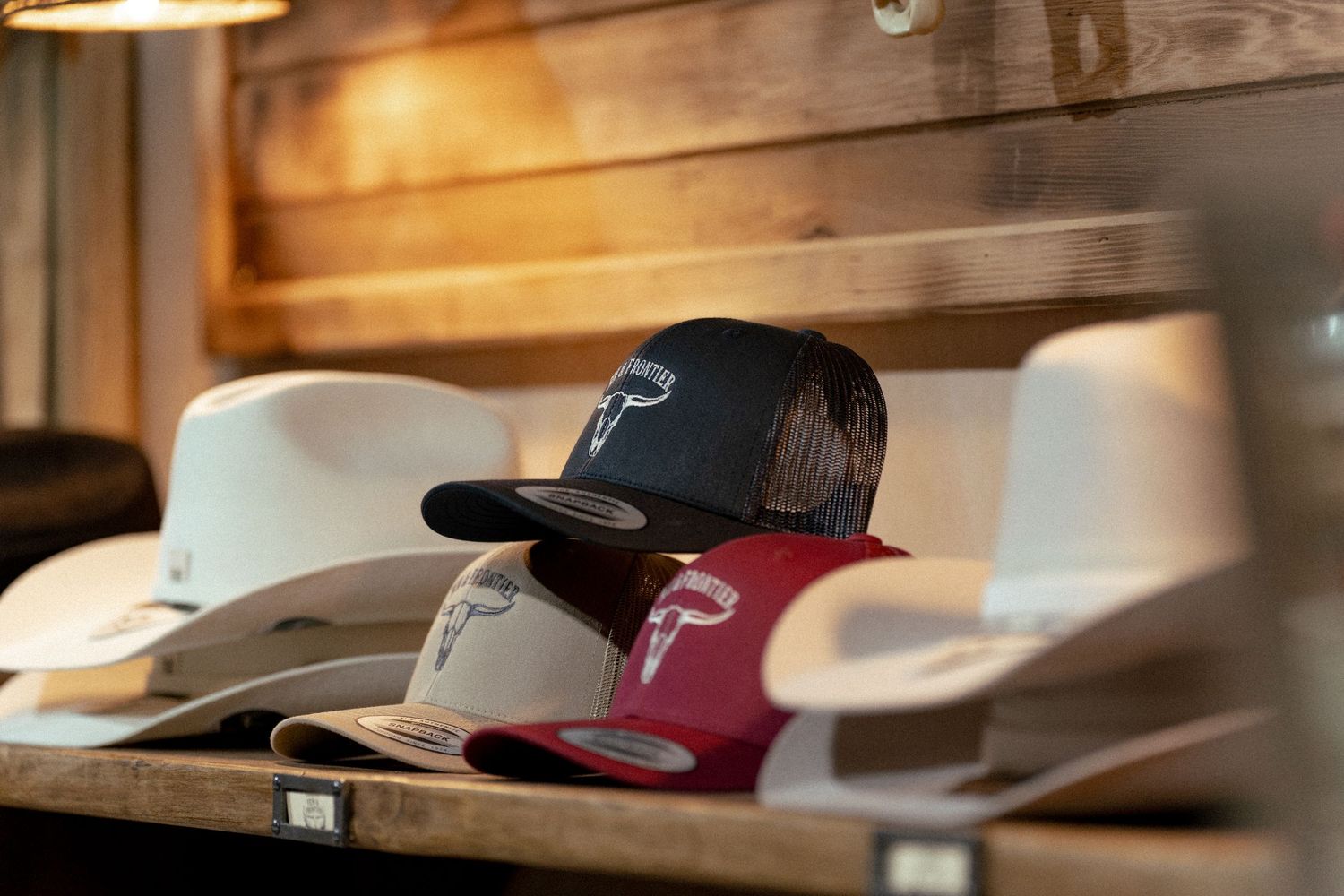Collection of western hats and trucker caps displayed on a rustic wooden shelf in a western wear store.