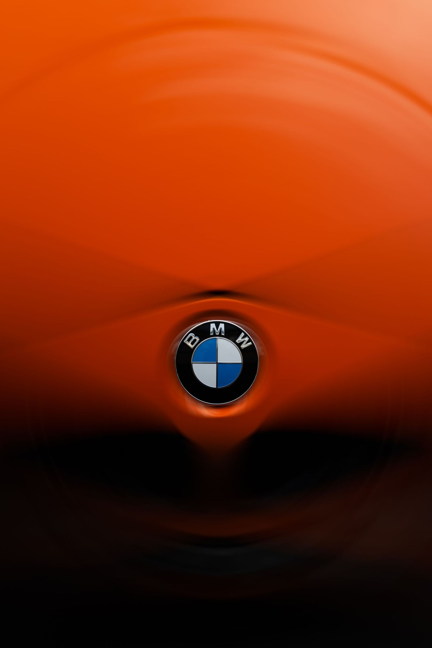 Close-up of a BMW logo emblem centered on a glossy orange car hood with ripple-like reflections.