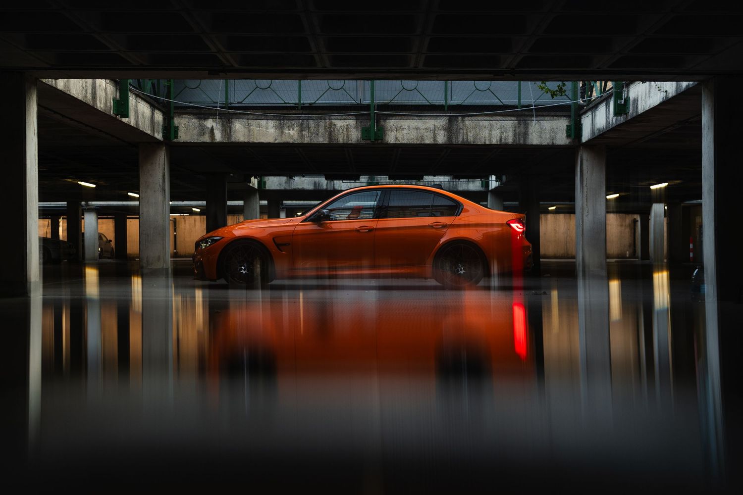Orange BMW sedan parked in a modern building garage, reflecting light on a wet floor.