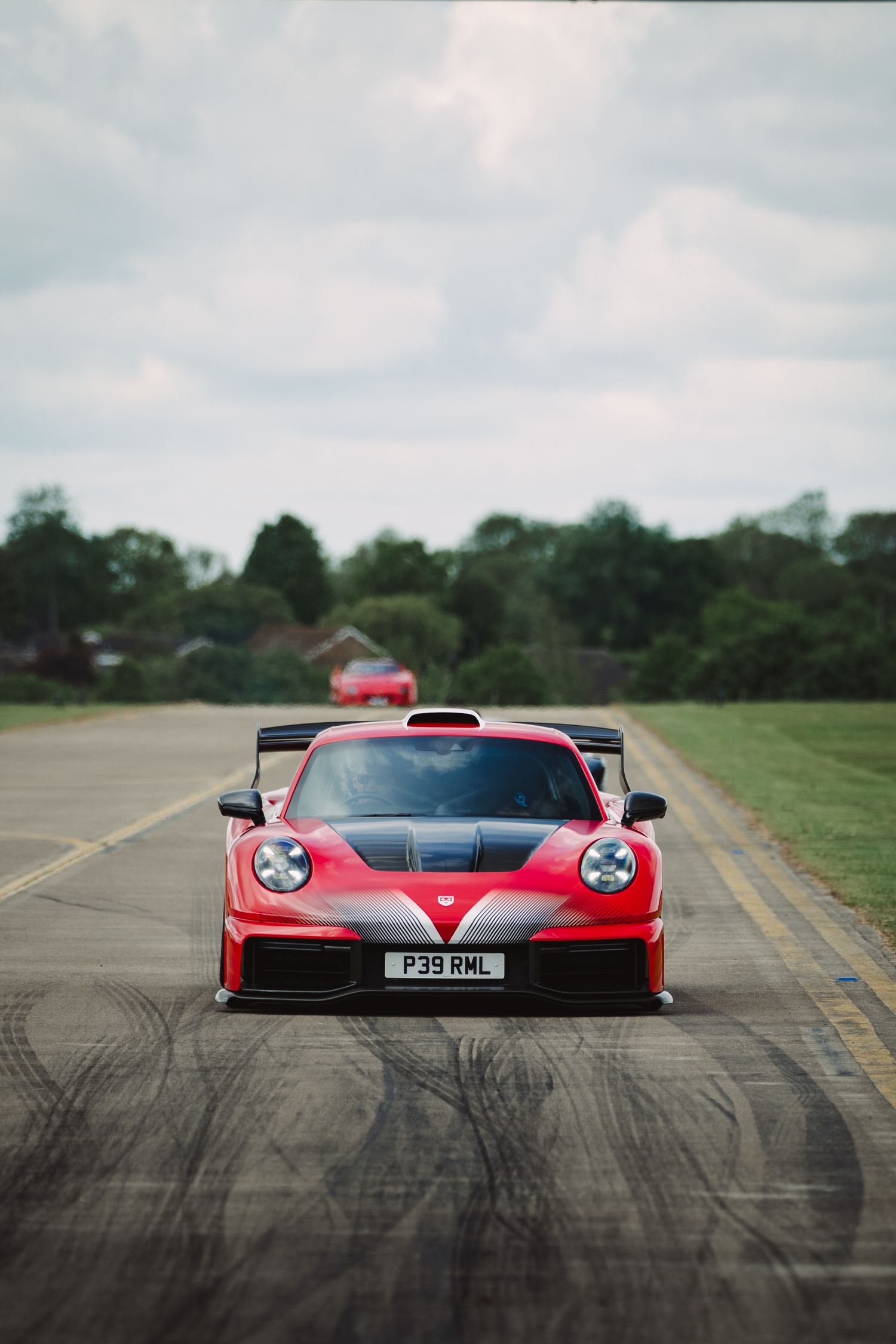 Red Porsche 911 GT3 RS with carbon accents on a runway, featuring a large rear wing and UK license plate P39 RWL.