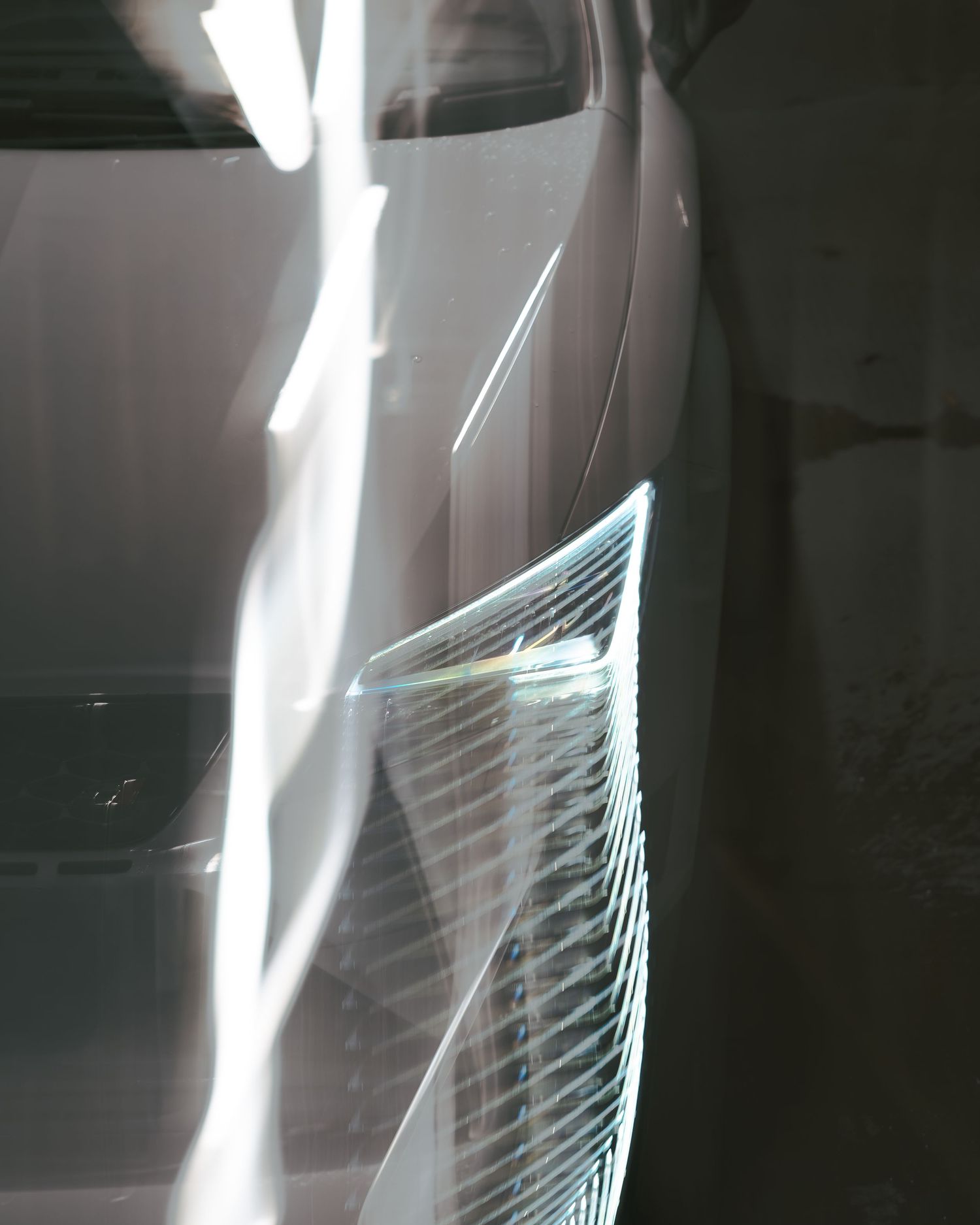 Detail shot of a white sports car side panel reflecting light in a dimly lit parking structure.