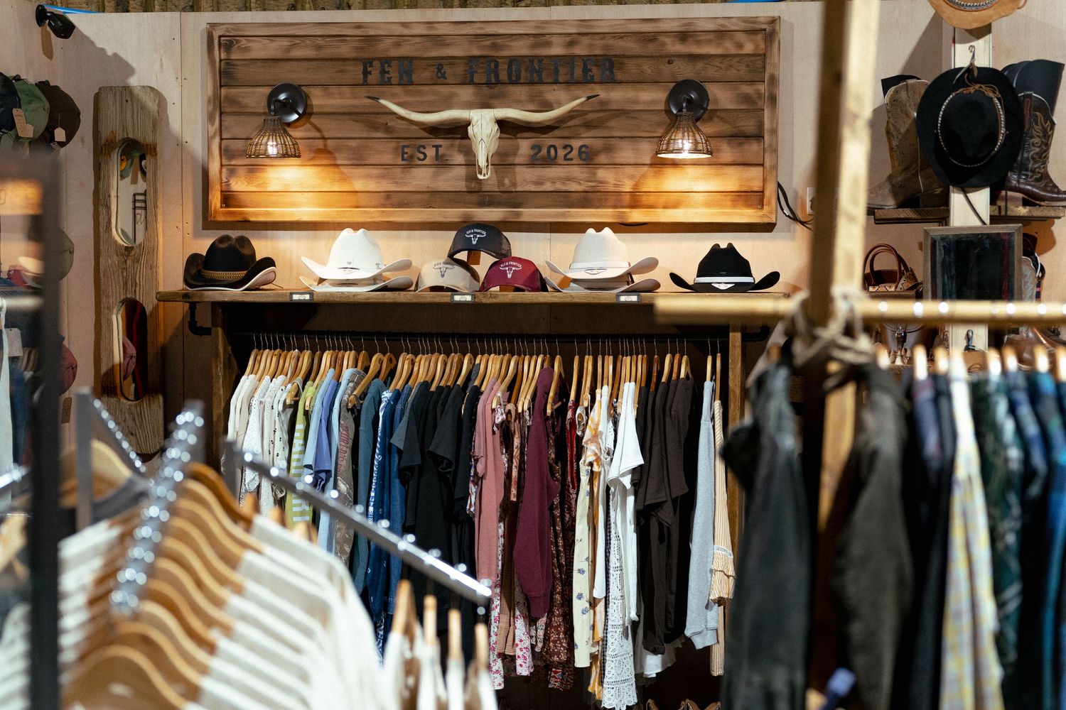 Western clothing store interior with cowboy hats, denim, and a rustic wood sign featuring a longhorn skull.