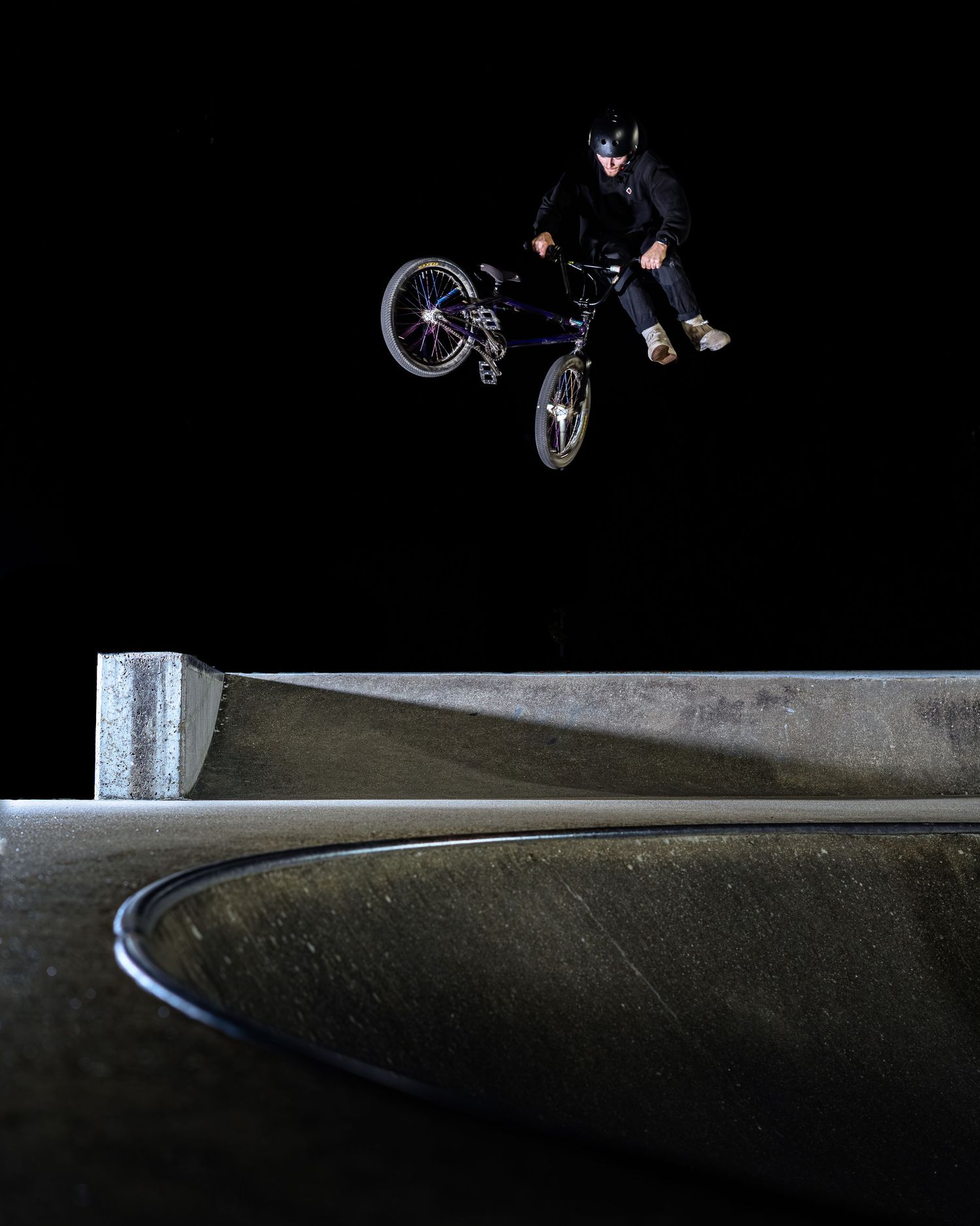 BMX rider catching big air over a concrete skatepark ramp during nighttime session.