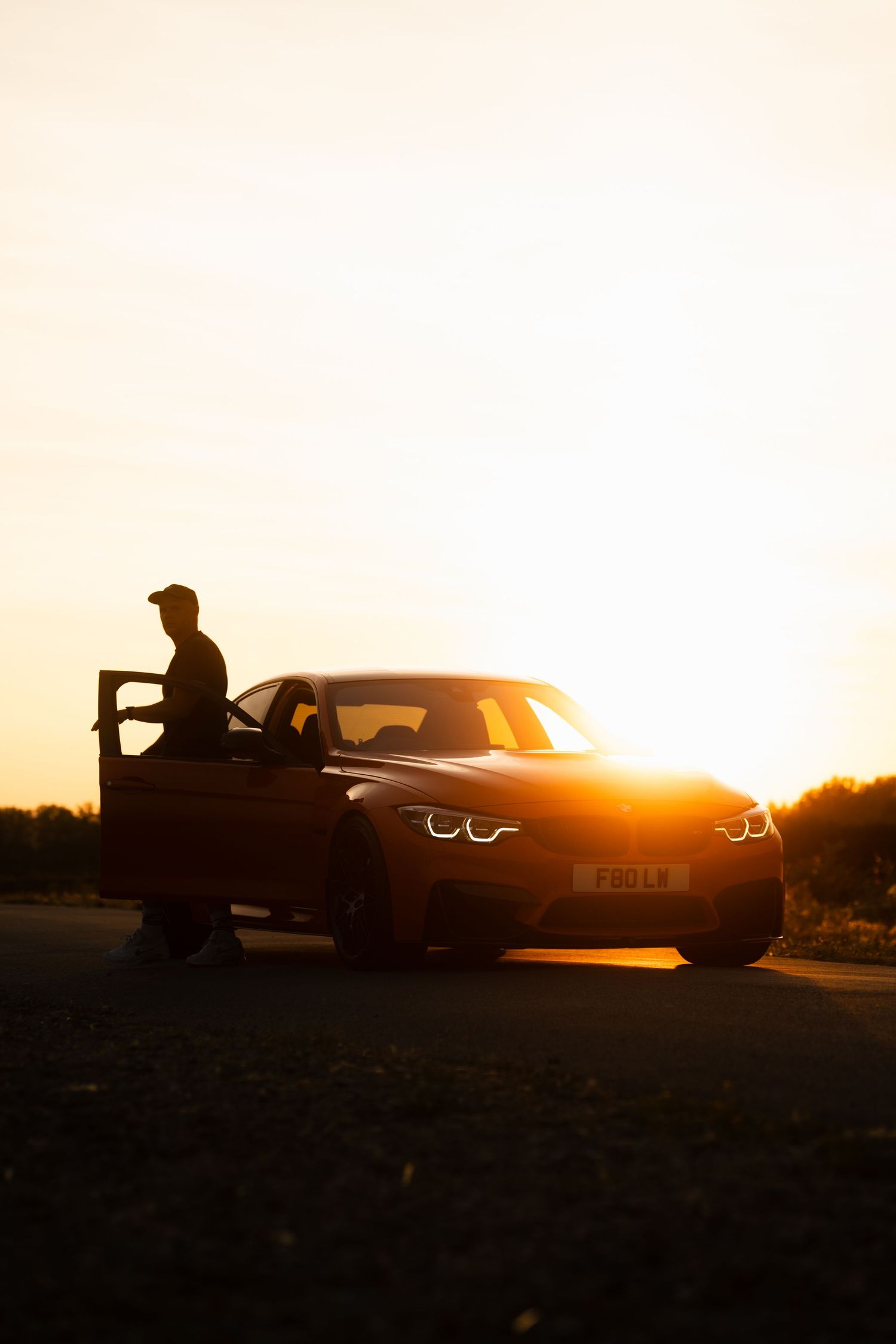 Silhouette of a man entering a BMW sports car at golden sunset on an open road.