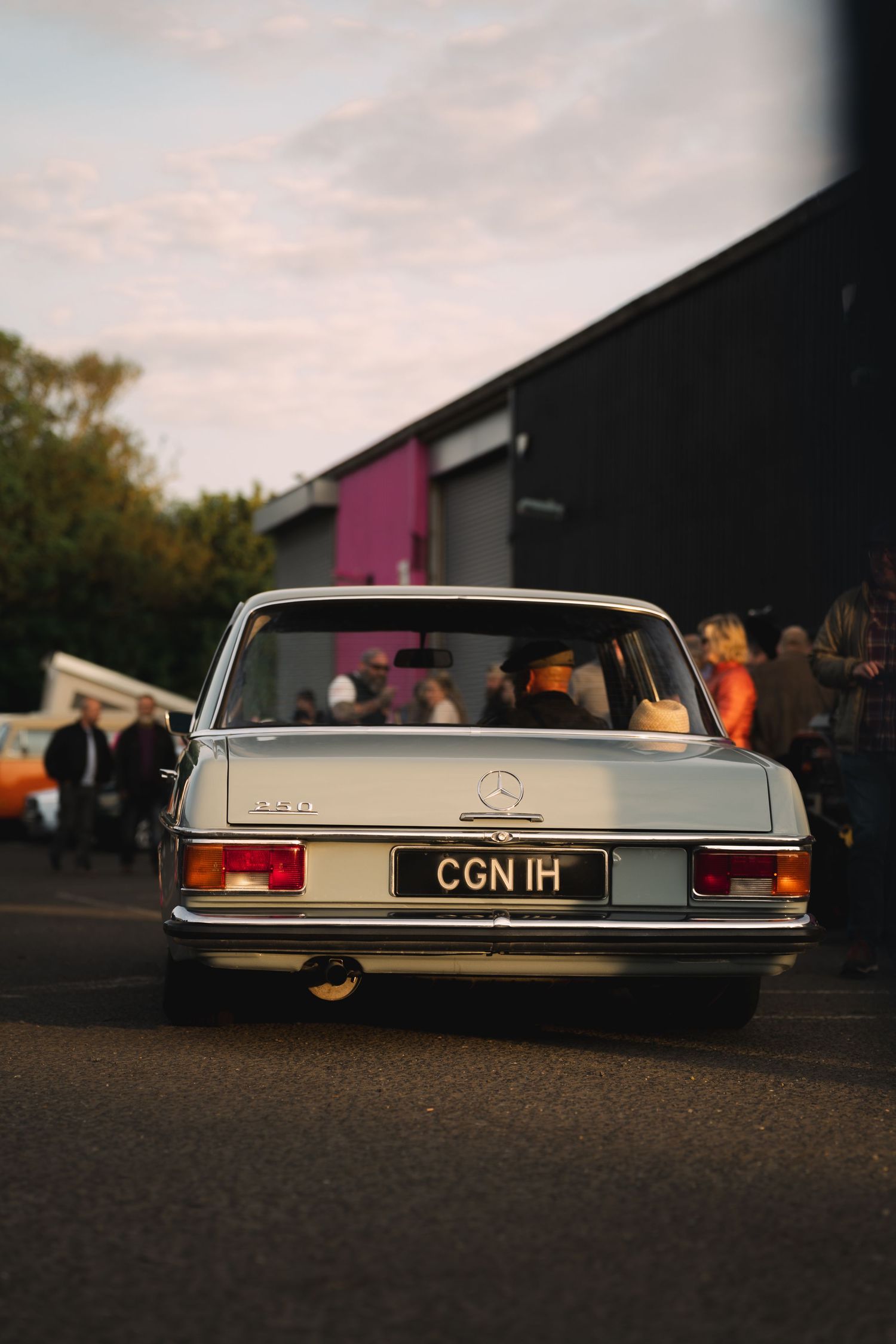 Rear view of a classic white Mercedes-Benz with license plate CGN 1H parked at dusk near a building.