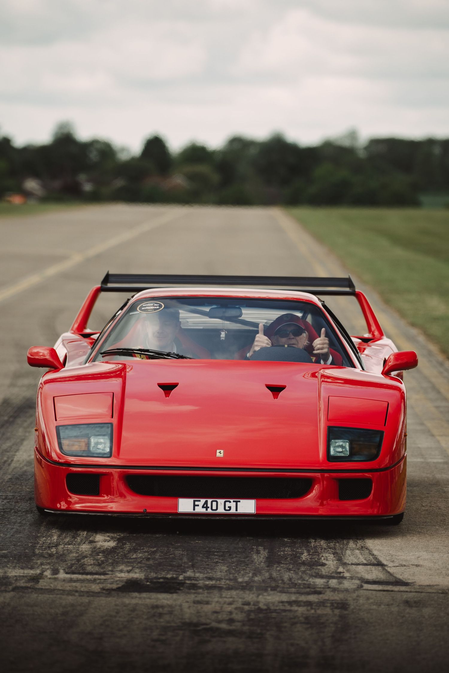 Red Ferrari F40 GT supercar on a runway, front view showing iconic pop-up headlights and large rear wing.