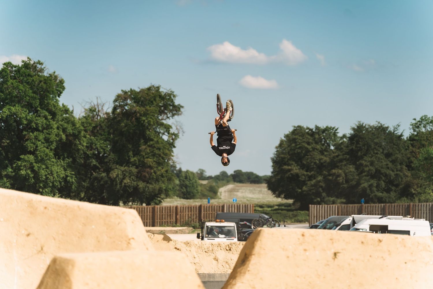 A BMX rider performs an inverted aerial trick high above sandy dirt jumps outdoors.