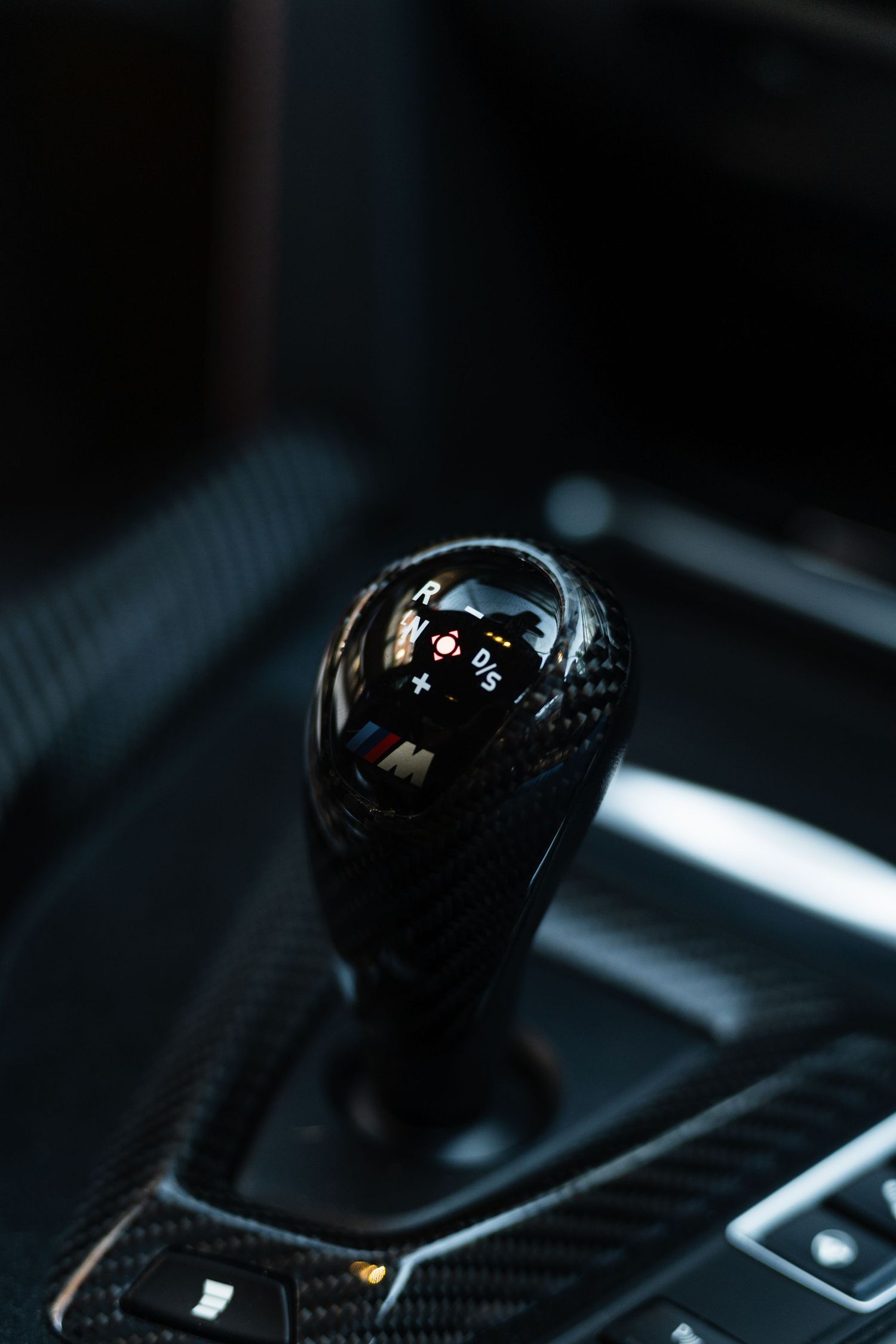 Close-up of a BMW M carbon fiber manual gear shift knob inside a luxury sports car interior.