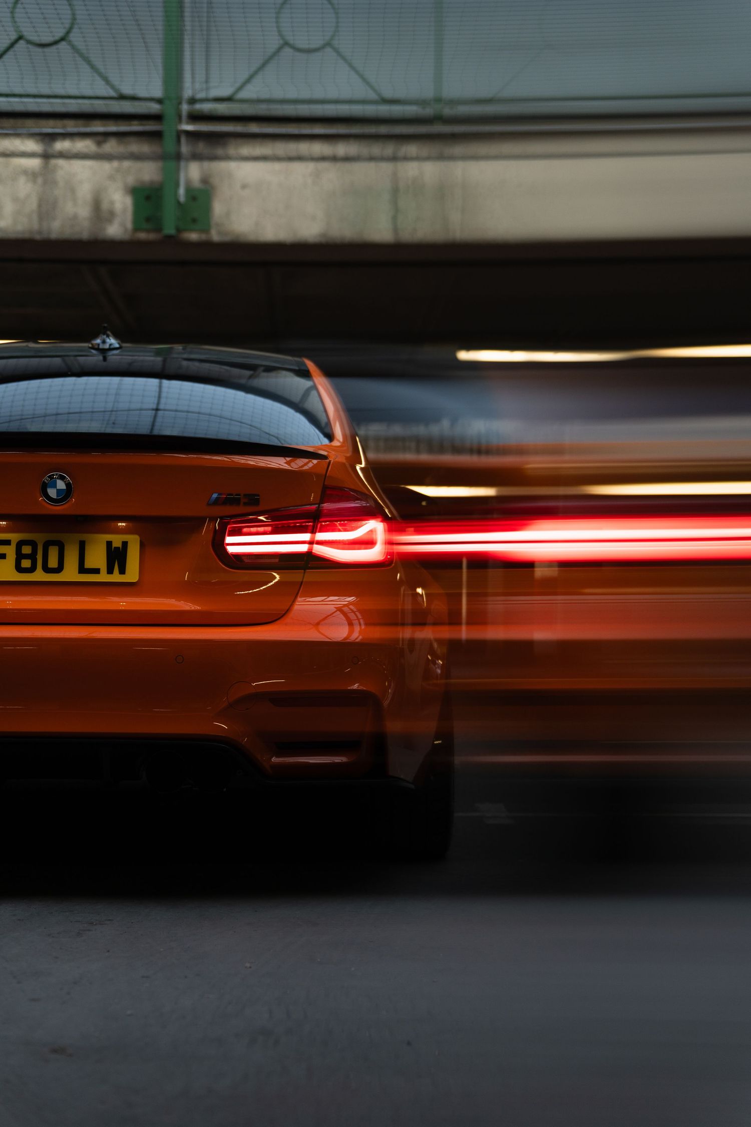 Orange BMW M3 F80 captured with motion blur effect, showcasing red tail lights glowing as it speeds through a tunnel.
