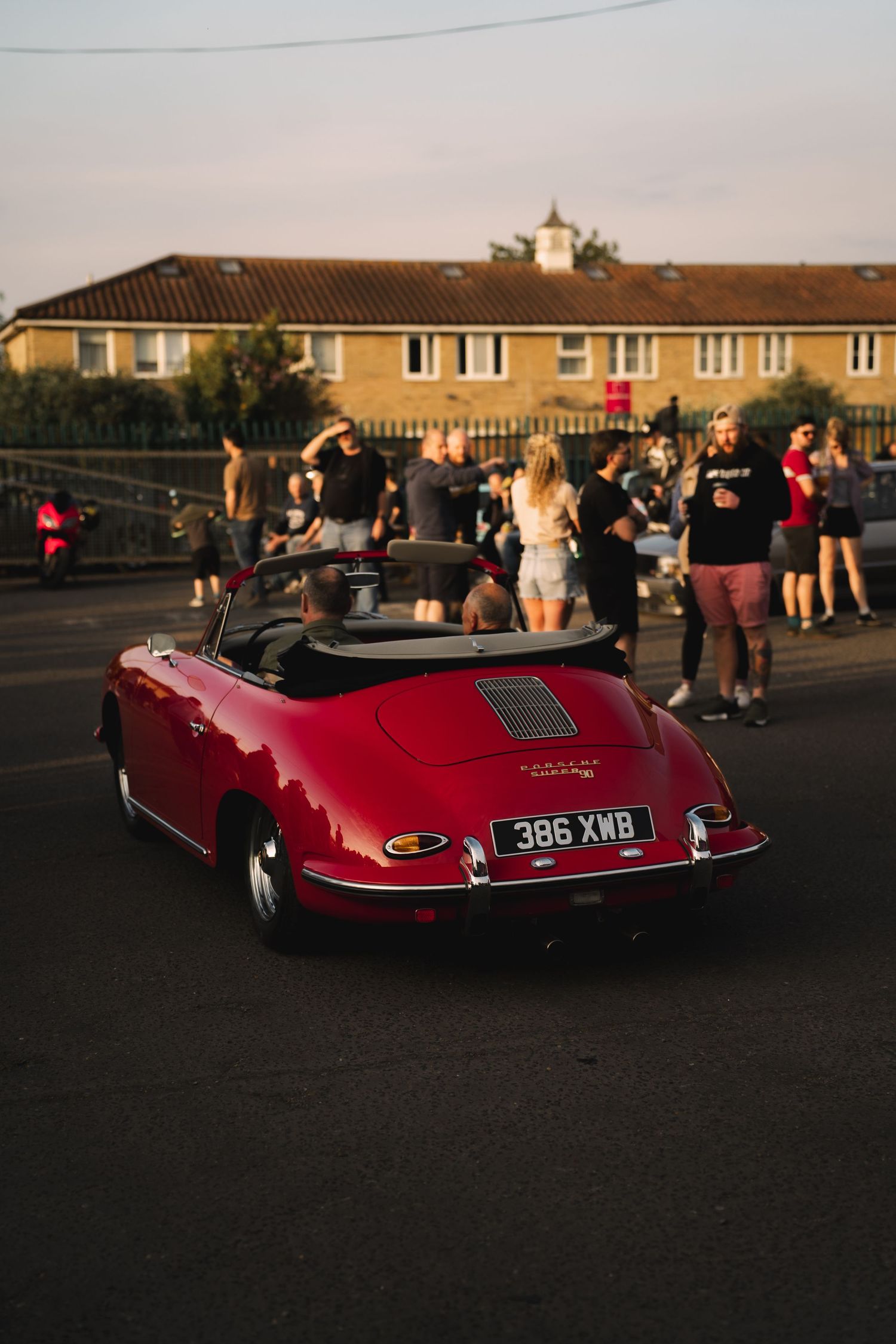 Rear view of a classic red Porsche 356 convertible with UK plate 386 XMB at a sunset car meet.