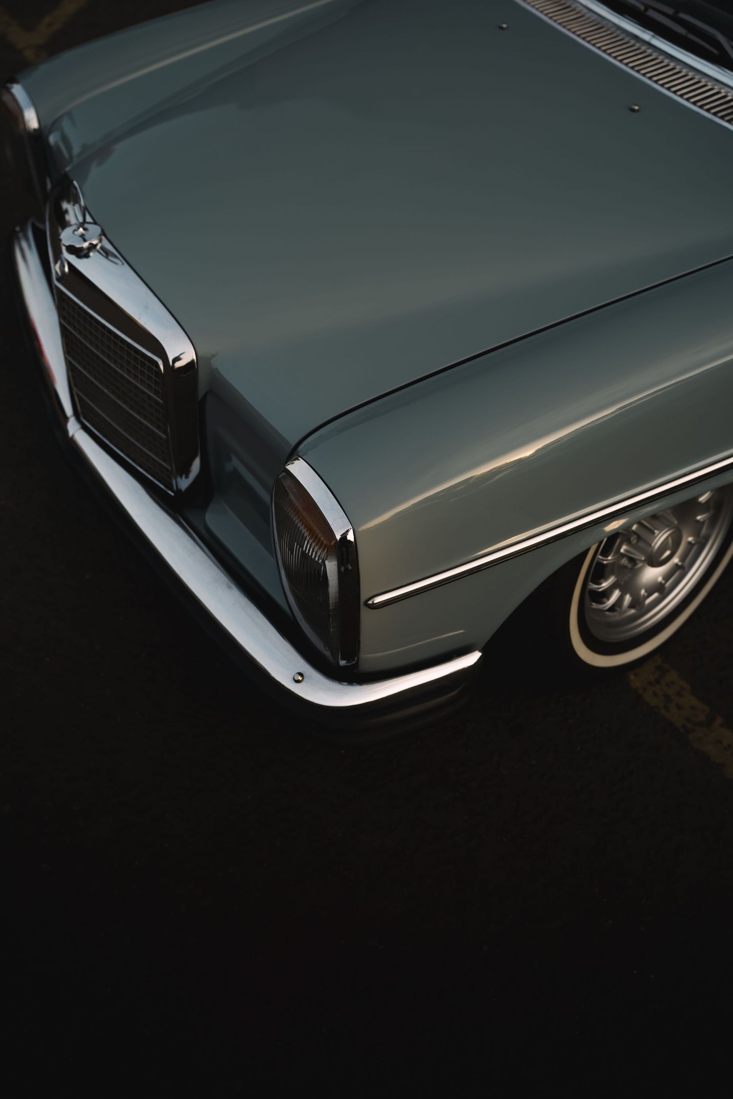 Vintage Mercedes-Benz classic car in silver-gray with whitewall tires, shot from above at a dark parking lot.