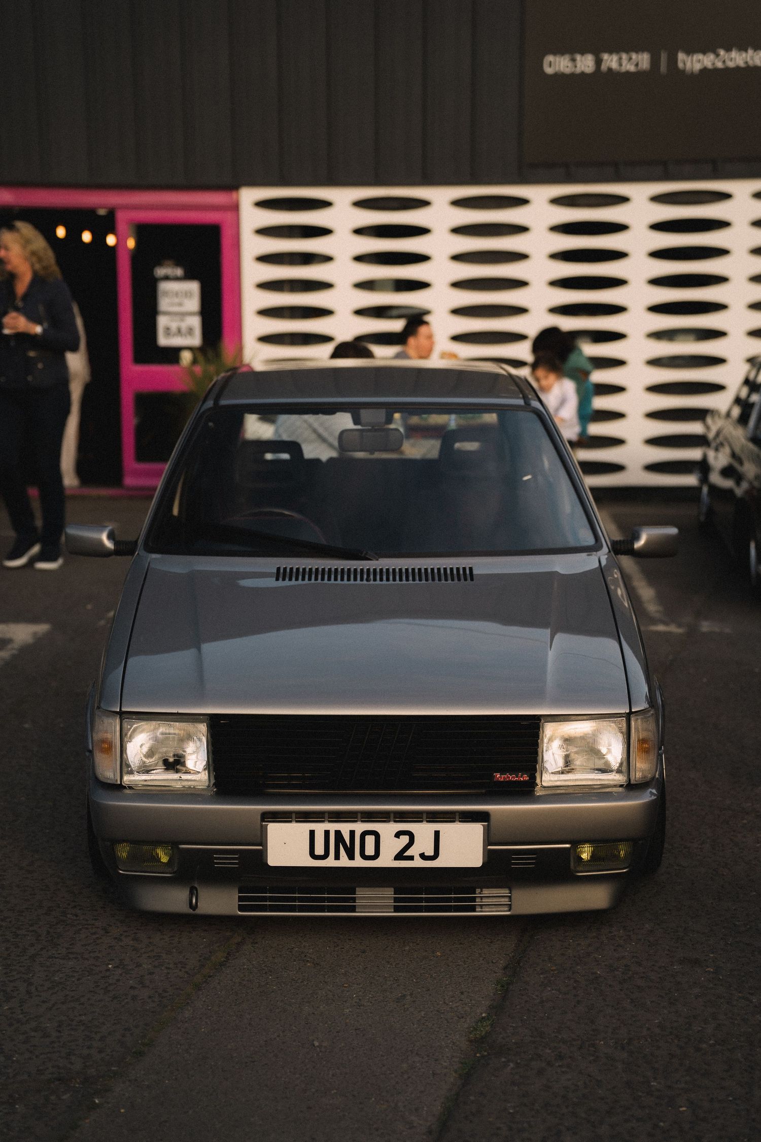 Gray Fiat Uno with UNO 2J license plate parked at a car meet, front view at dusk.