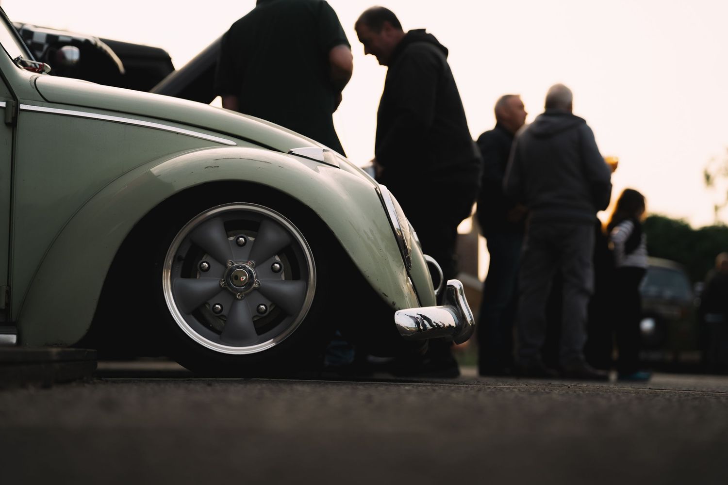 Lowered vintage VW Beetle with polished wheels at a classic car meet during sunset.