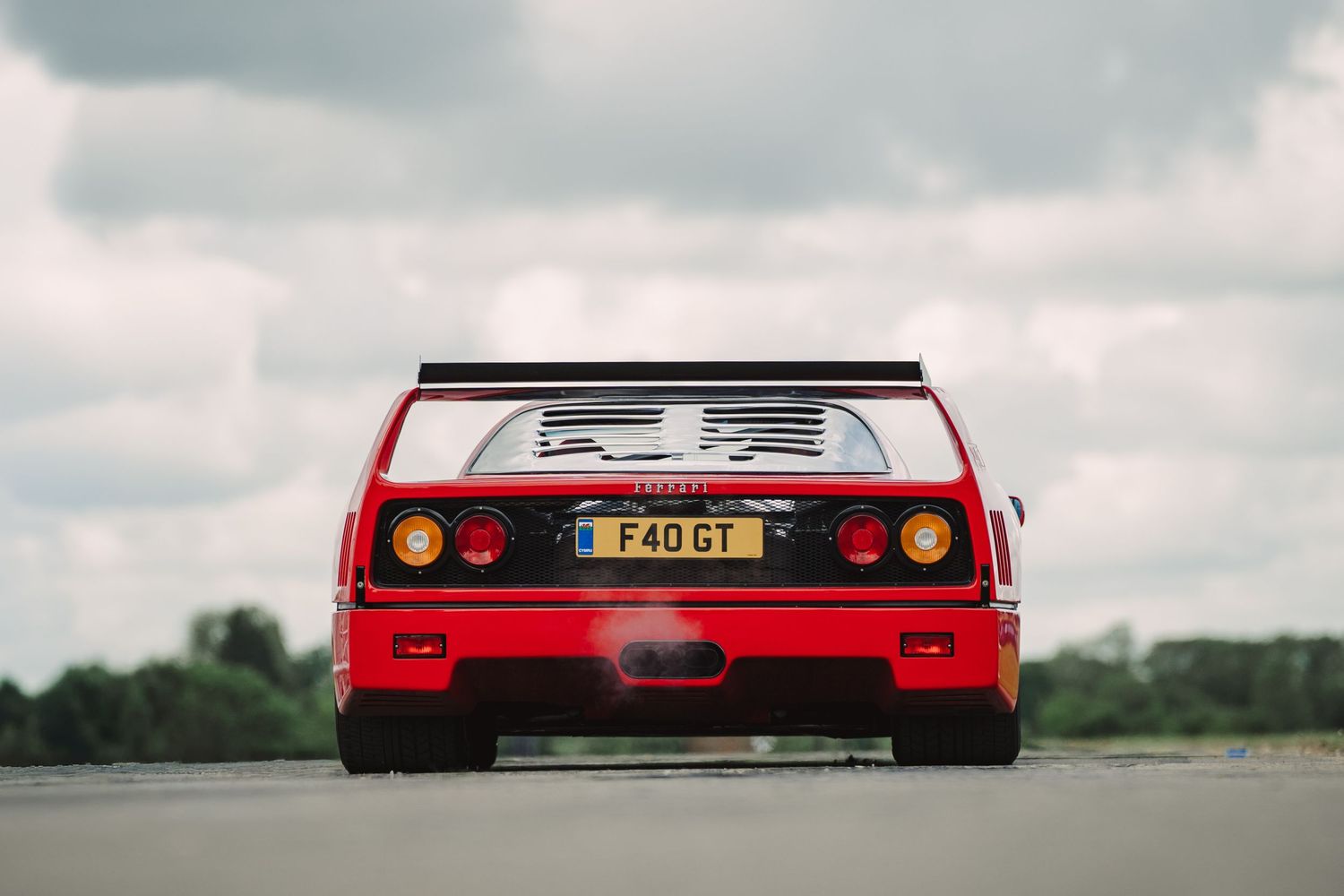 Red Ferrari F40 GT supercar rear view on track, featuring iconic wing spoiler and yellow UK license plate.