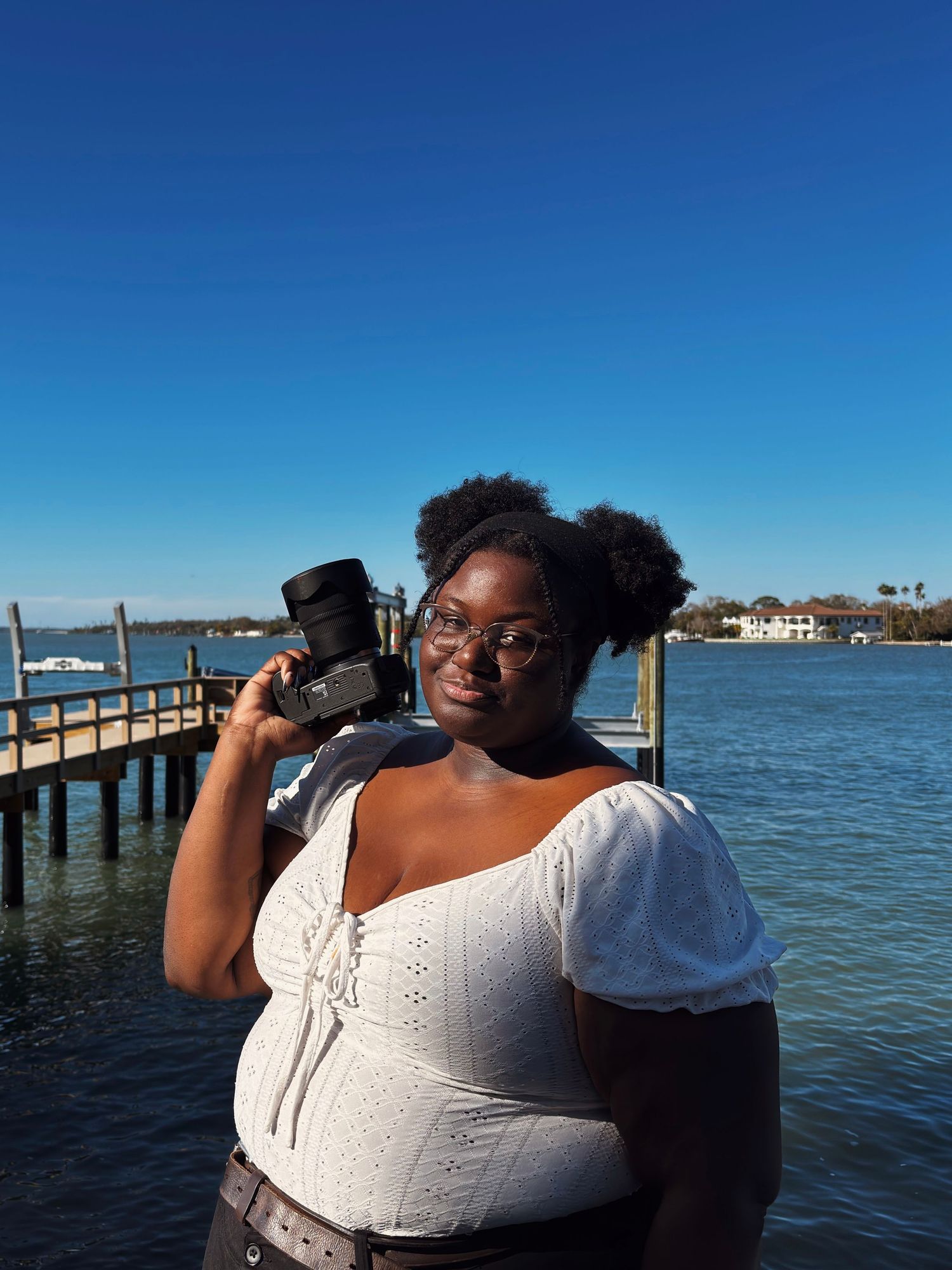 Someone in a white top gazes out over blue waters from a wooden pier on a sunny day.