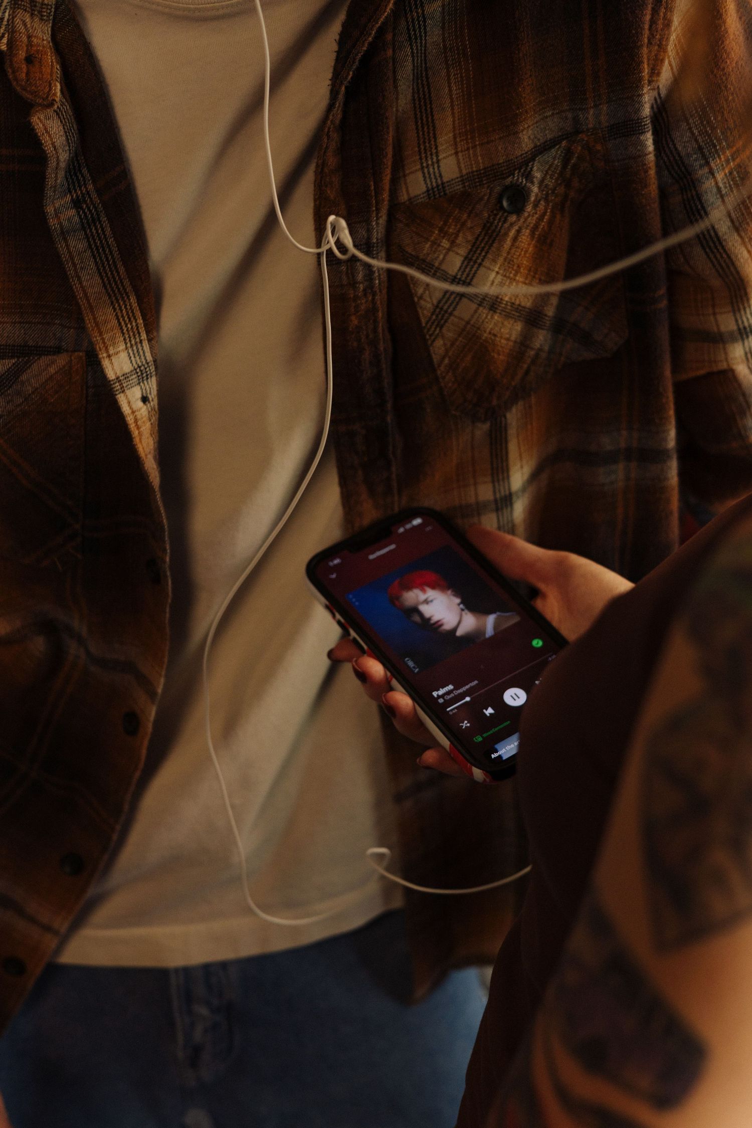 Person holding smartphone in dark setting with white earbuds or headphone cables visible.