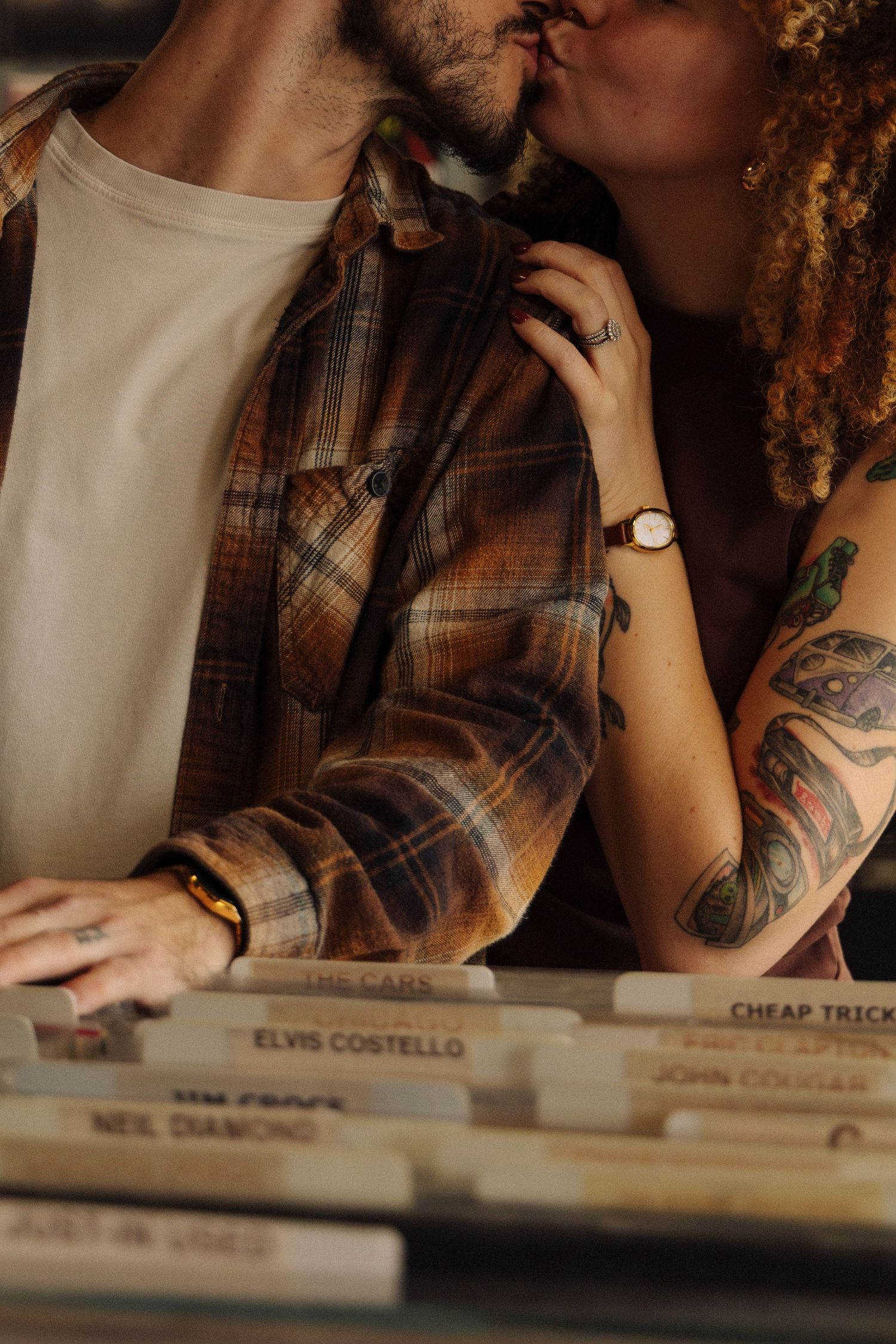 Person with tattoos browsing through vinyl records including Elvis Costello and Cheap Trick albums.