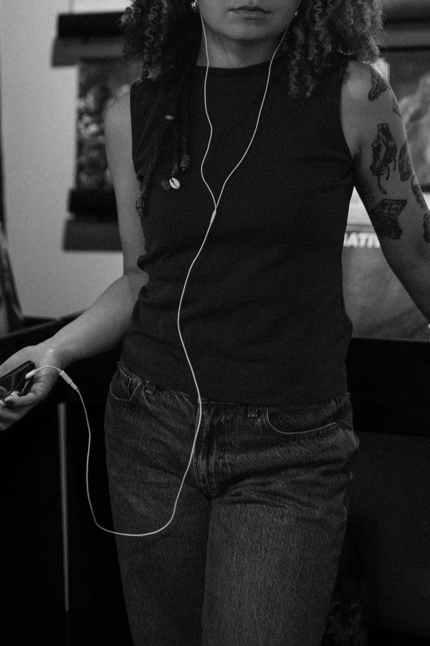 Person in dark clothing wearing white earbuds stands against dark background in black and white photo series.