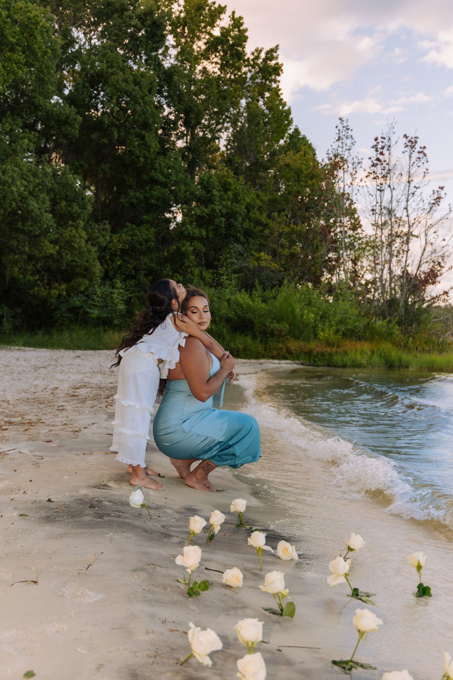 A beach scene with white roses scattered on the sand at sunset.