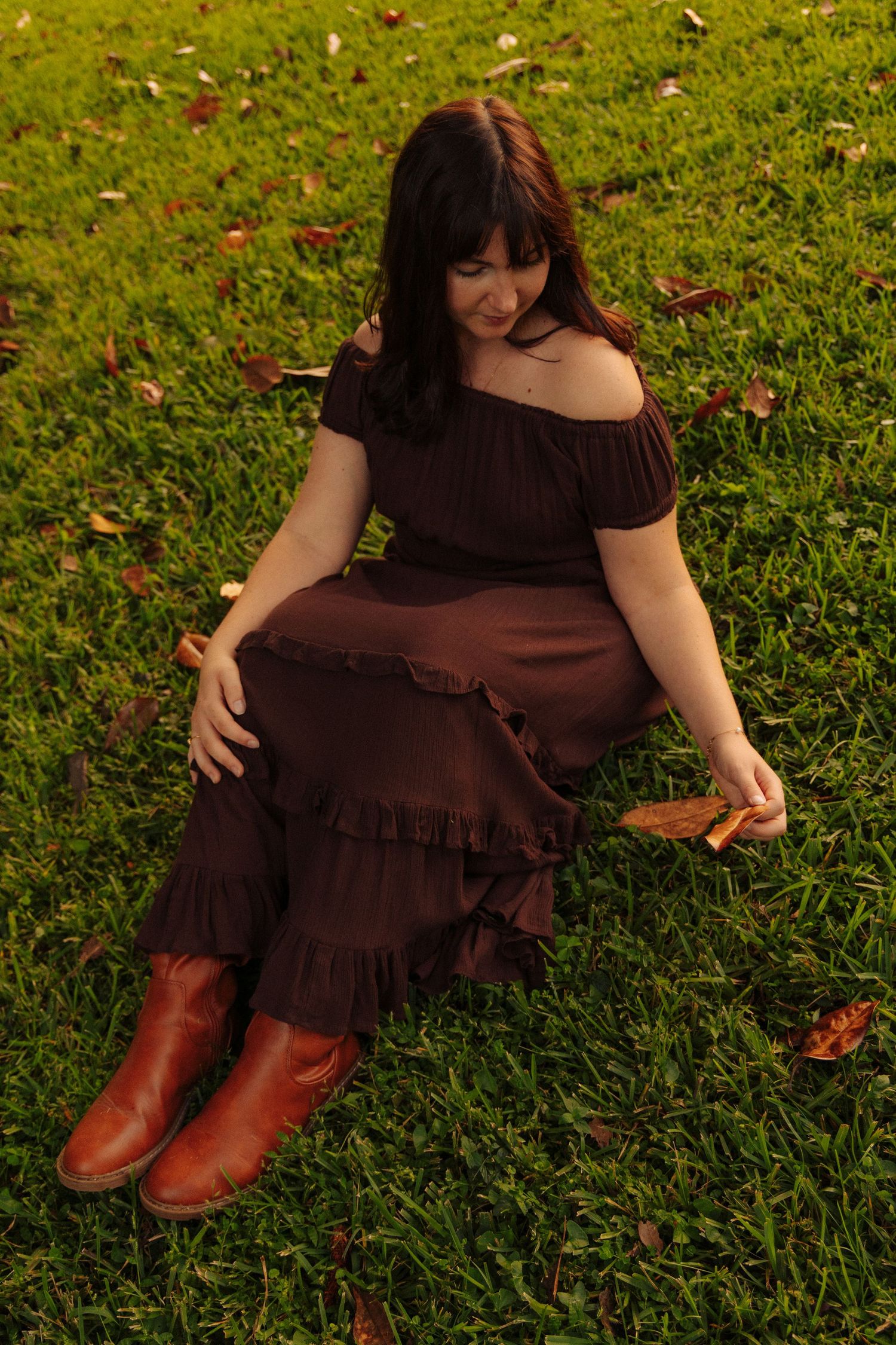 Person in brown dress relaxes on grass with autumn leaves in artistic portrait sequence.